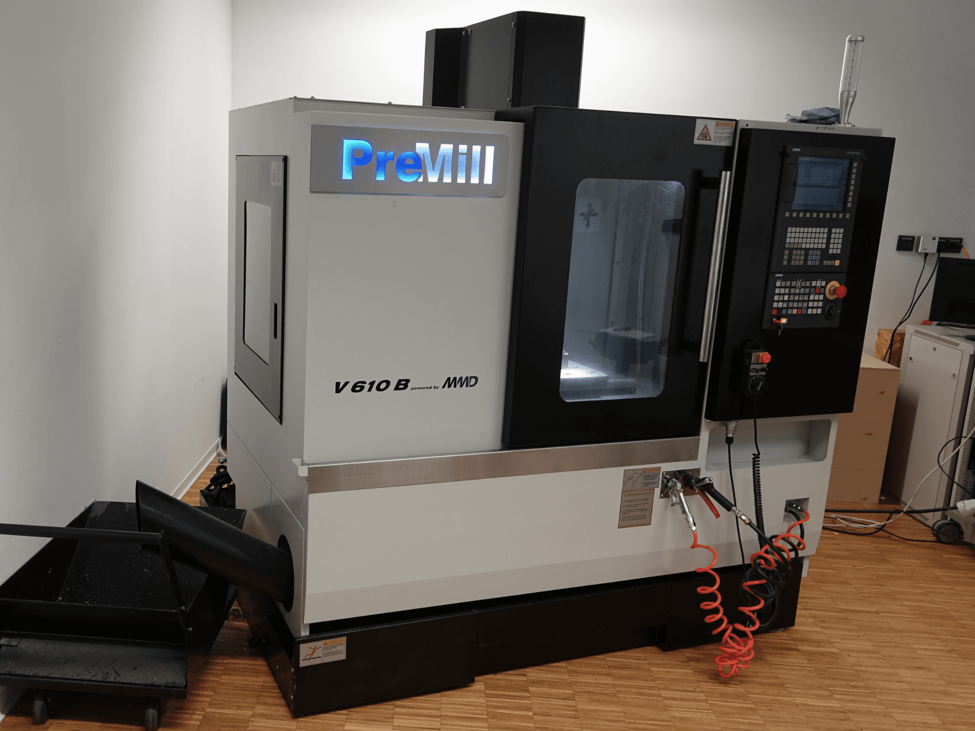 Centre d'usinage vertical PreMill V 610 B, vue de face, avec panneau de commande, système de refroidissement et flexibles d'air raccordés.