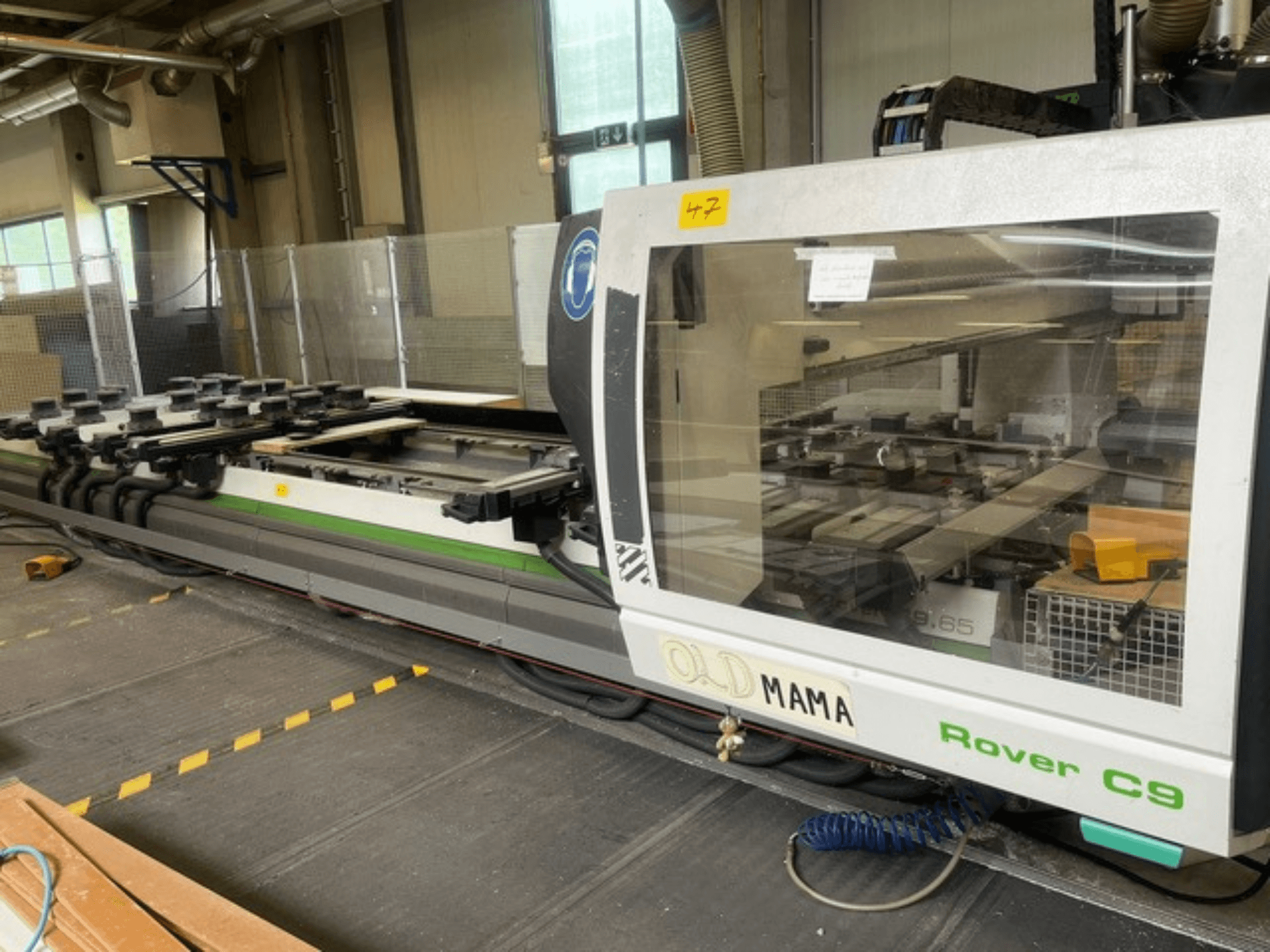 Défonceuse CNC BIESSE Rover C 9.65 dans un atelier, vue latérale montrant le panneau de commande et la table de travail avec des pinces.