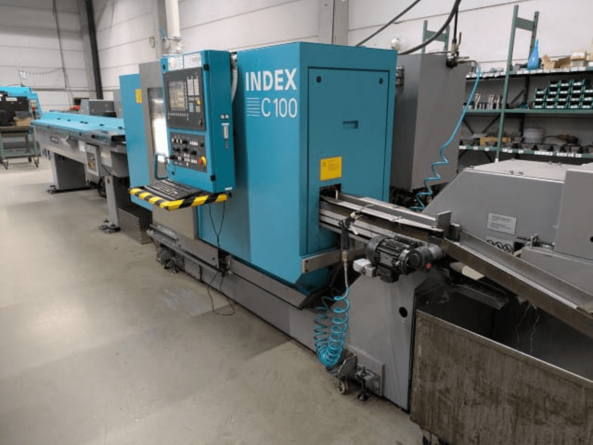 Machine à tourner horizontale Index C100, vue de profil ; équipée d'un panneau de commande, d'un système d'avance et d'un bac de récupération des copeaux métalliques.