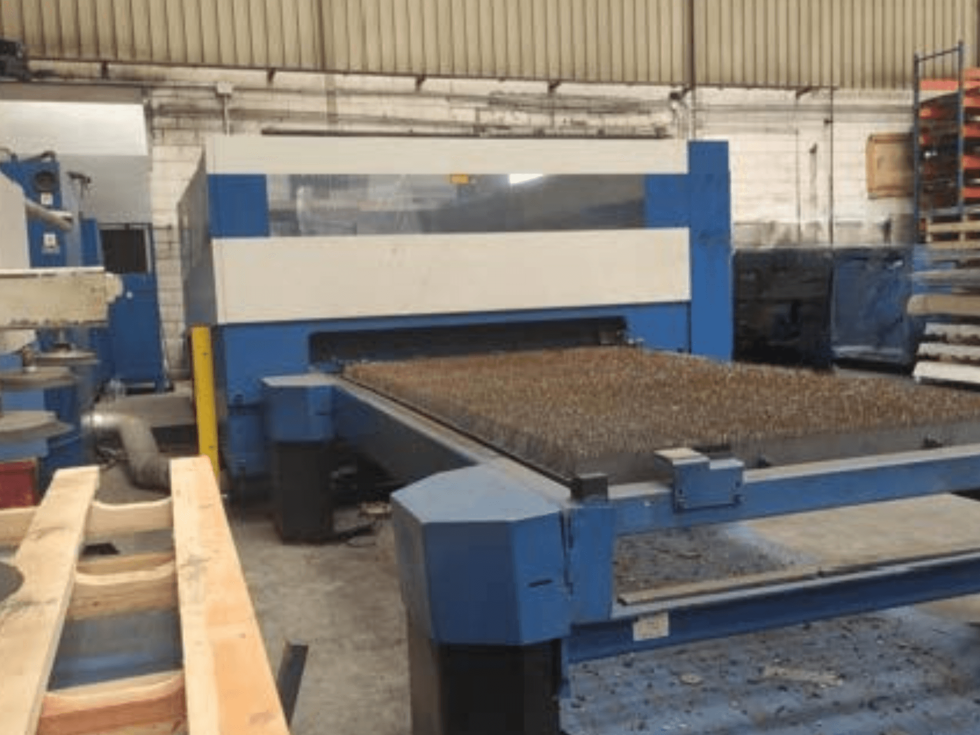 Machine de découpe laser bleue avec un lit en métal texturé, vue de côté, montrant l'installation opérationnelle dans un espace de travail industriel.