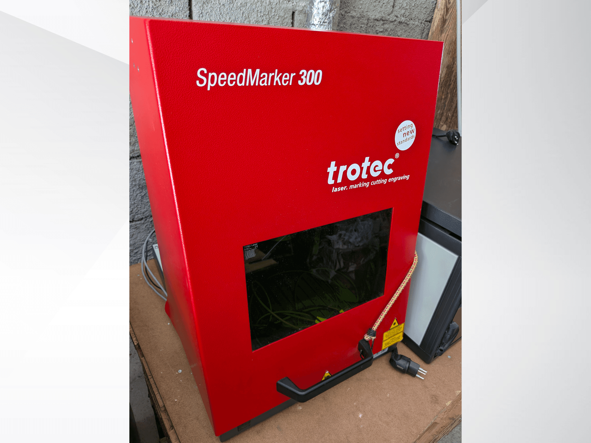 Machine de marquage laser rouge Trotec SpeedMarker 300 vue de face, avec une grande fenêtre de visualisation et un branchement électrique.