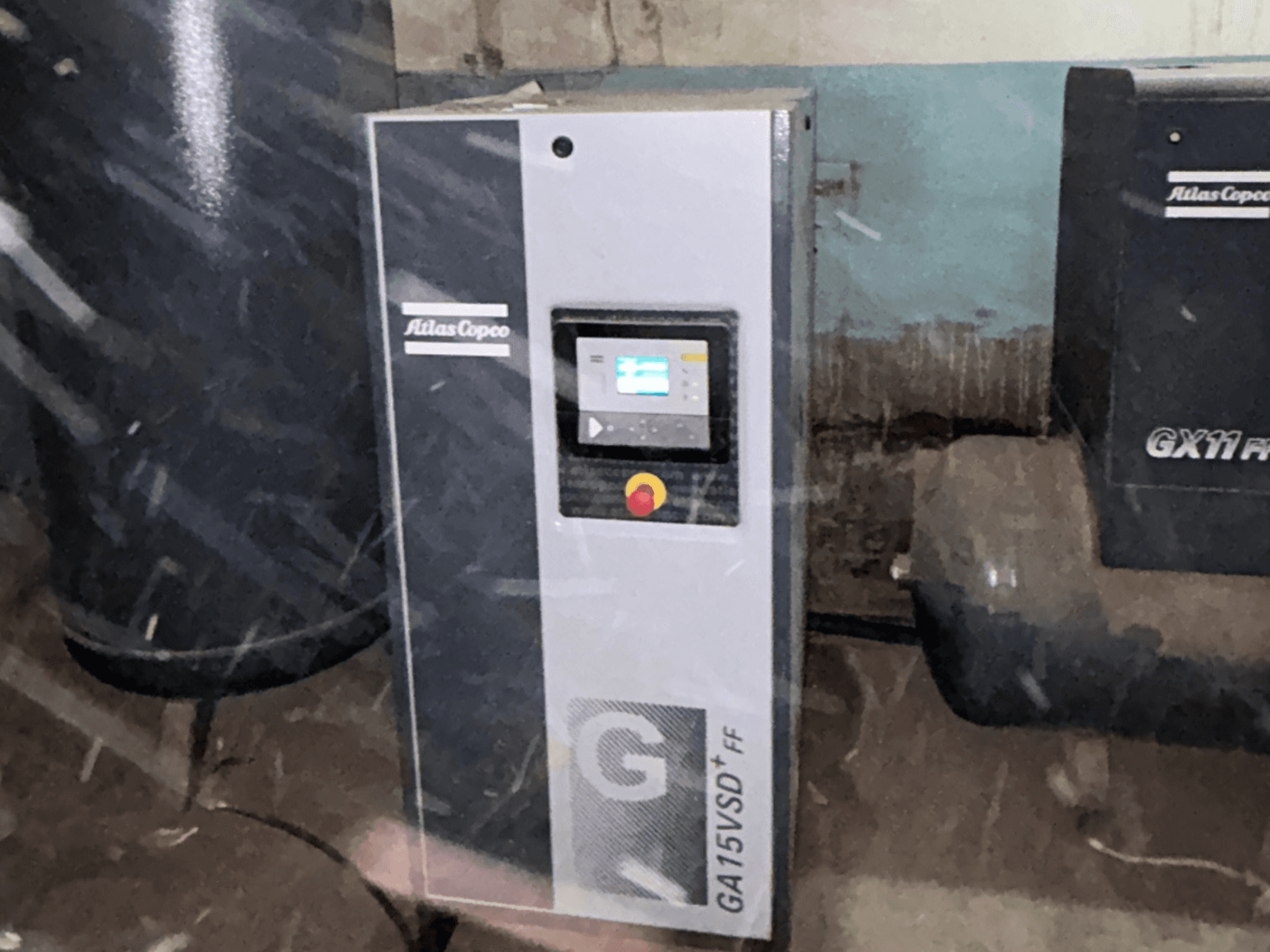 Compresseur d'air Atlas Copco GA15VSD+FF, vue de face, comprenant un panneau de commande avec écran et un bouton d'arrêt d'urgence rouge.