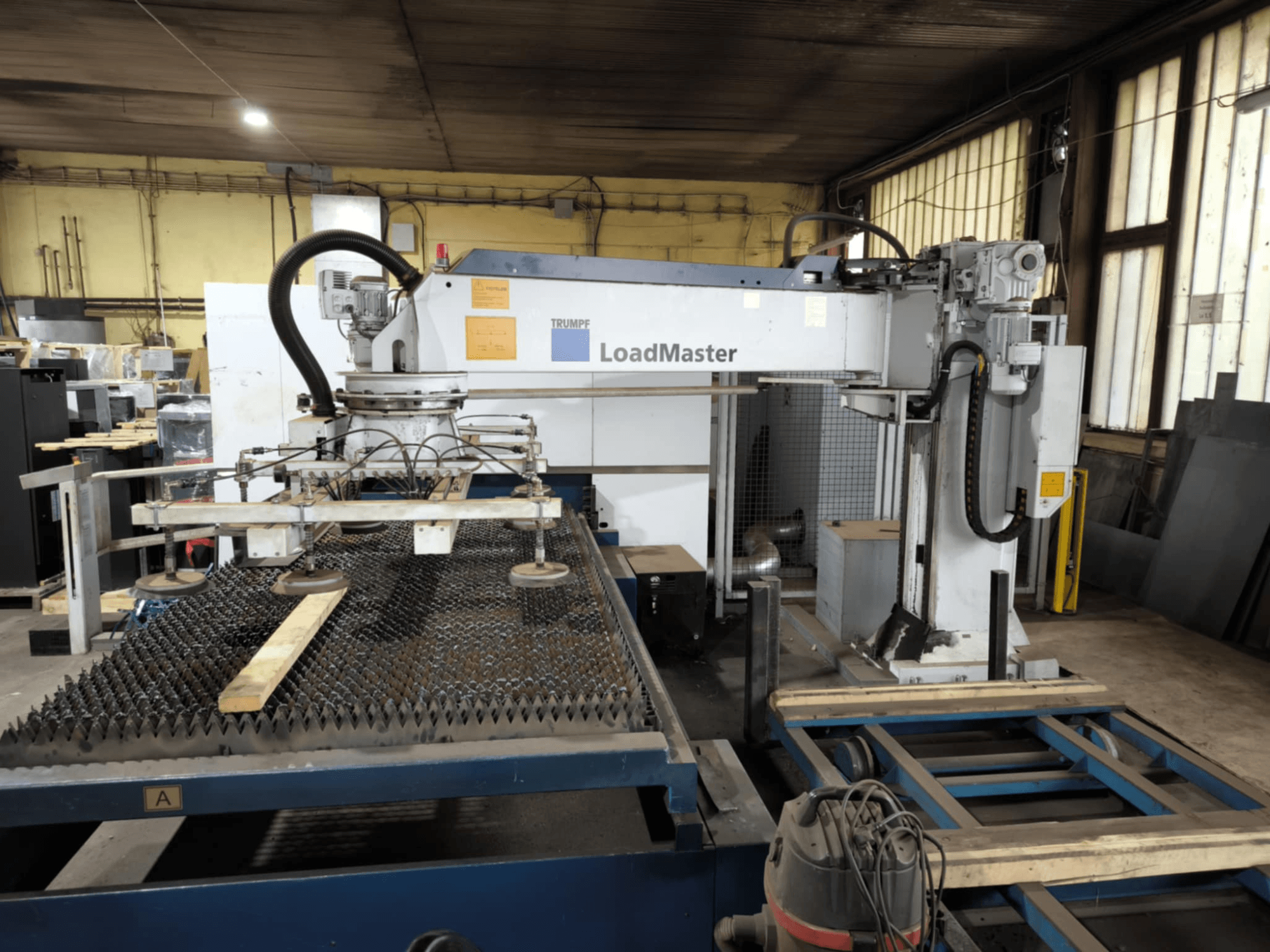 Machine de coupe TRUMPF TRULASER 3030 FIBER, vue de face, présentant le système LoadMaster et positionnée sur une table de travail caillebotis.