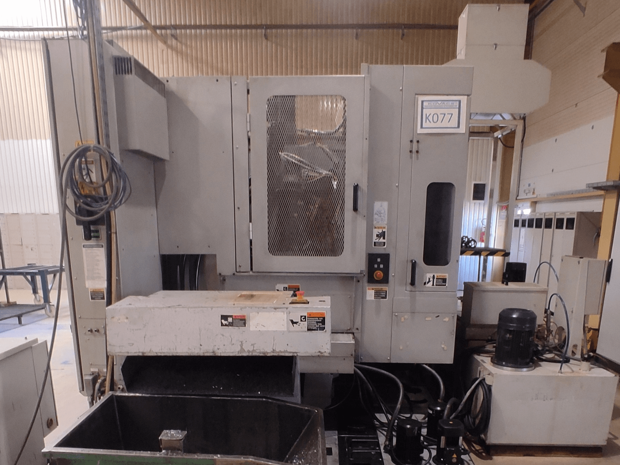 Machine CNC industrielle grise avec une grande table de travail, vue de côté, comportant un panneau de commande et un réservoir de liquide de refroidissement, modèle K077.