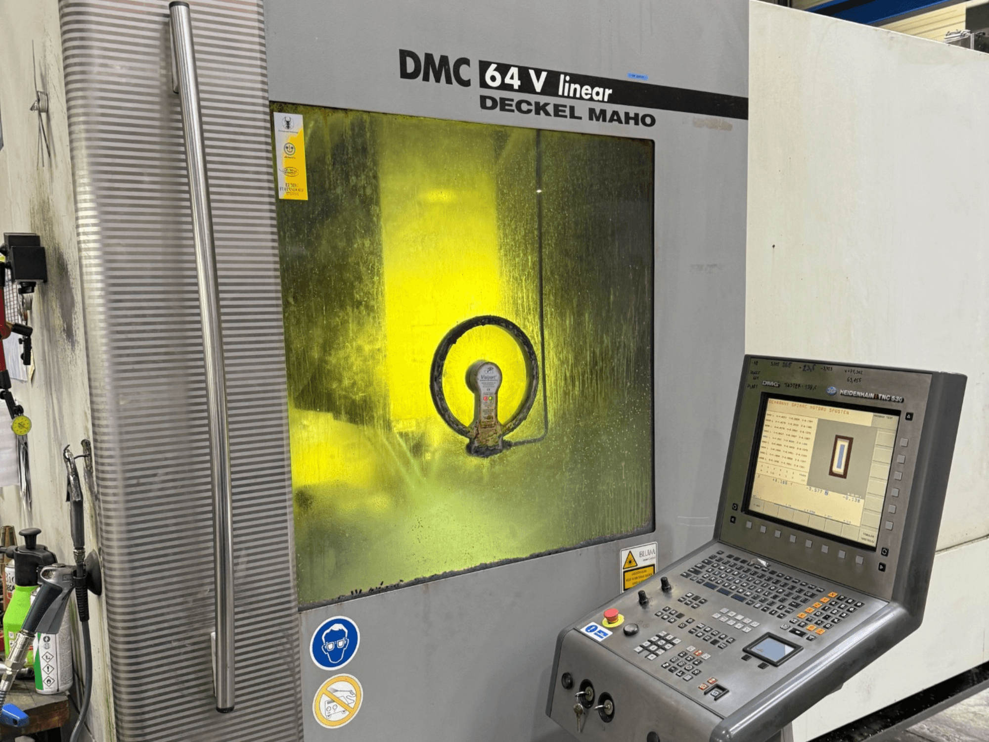 DMC 64 V linear by Deckel Maho, vue de face de la machine avec panneau de commande et fenêtre teintée en jaune montrant les mécanismes intérieurs.