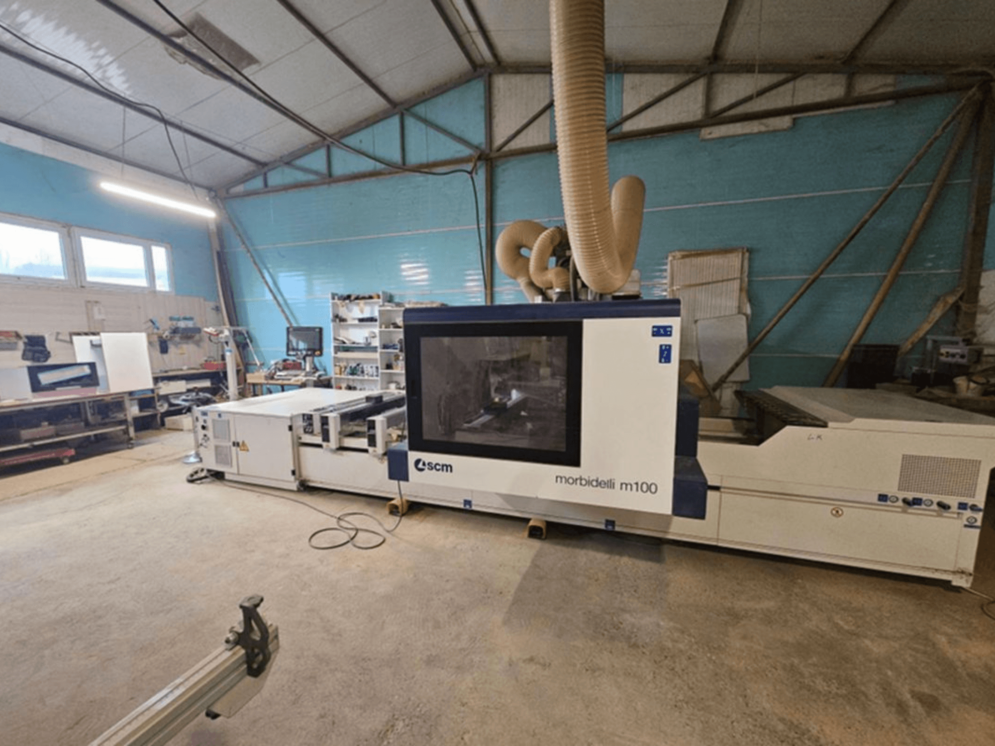 Centre d'usinage CNC SCM MORBIDELLI M 100 dans un atelier, vue de face avec système d'aspiration des poussières et équipement de l'espace de travail environnant.