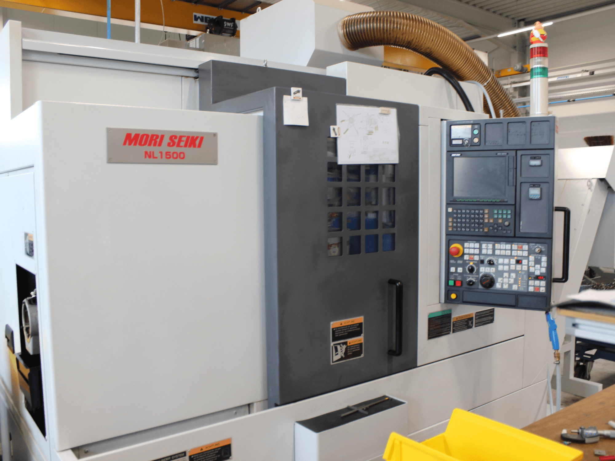 Centre de tournage-fraisage MORI SEIKI NL 1500 SY vu de profil, avec son panneau de commande, ses étiquettes de sécurité et son système de refroidissement.