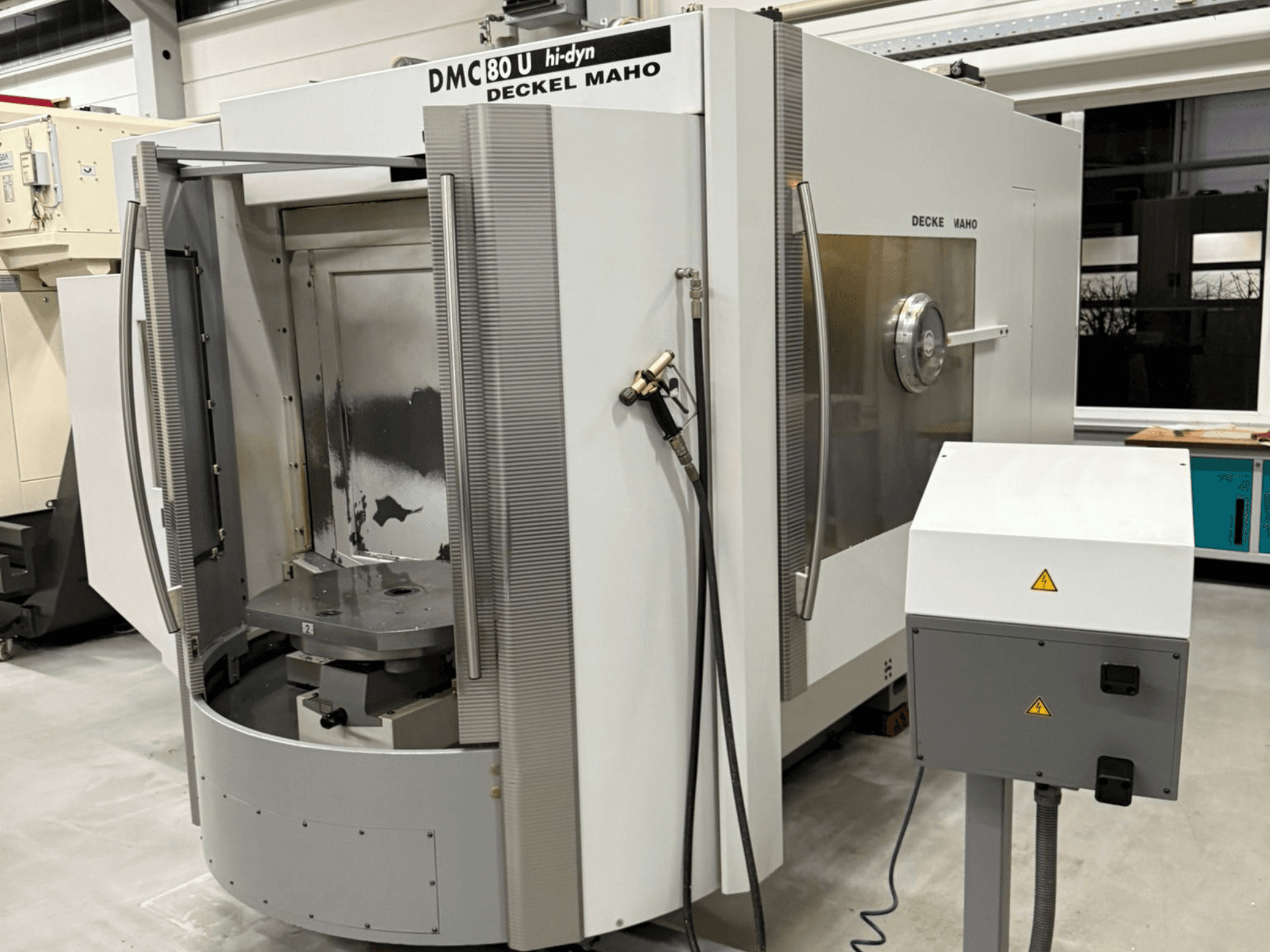 Vue de face d'une fraiseuse CNC à grande vitesse Deckel Maho DMC 80 U, avec une porte d'accès ouverte et un panneau de commande sur le côté.