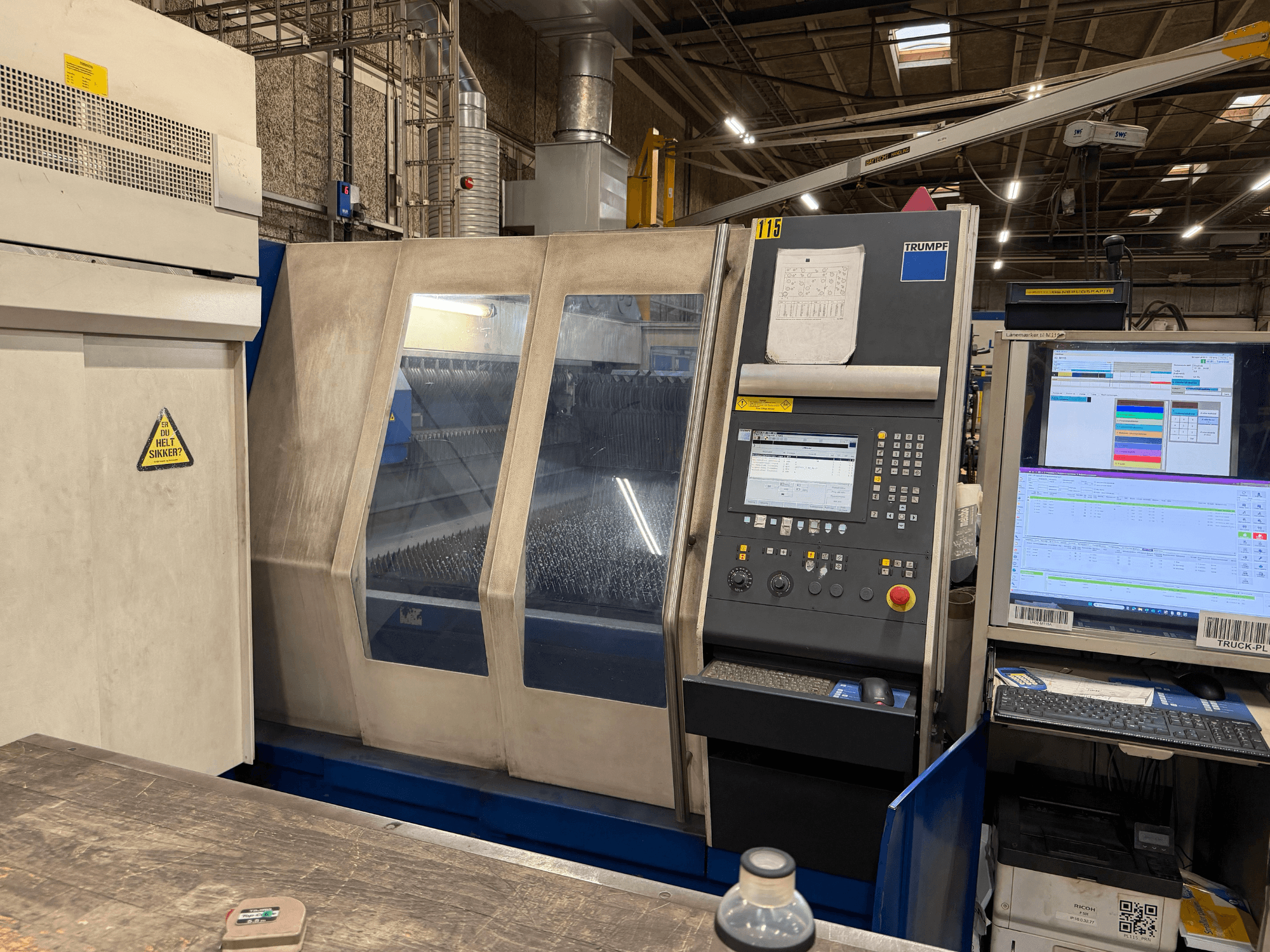 Vue de face d'une machine laser industrielle Trumpf avec panneau de commande et affichages numériques, installée dans un environnement industriel.