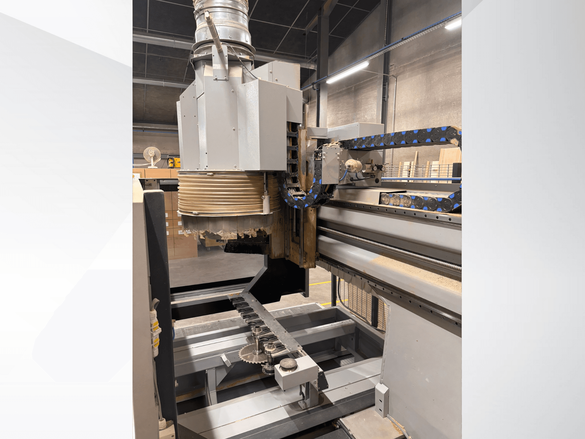 Toupie CNC avec une grande broche et un convoyeur, vue de côté, présentant des outils de coupe du bois et des composants de machines.