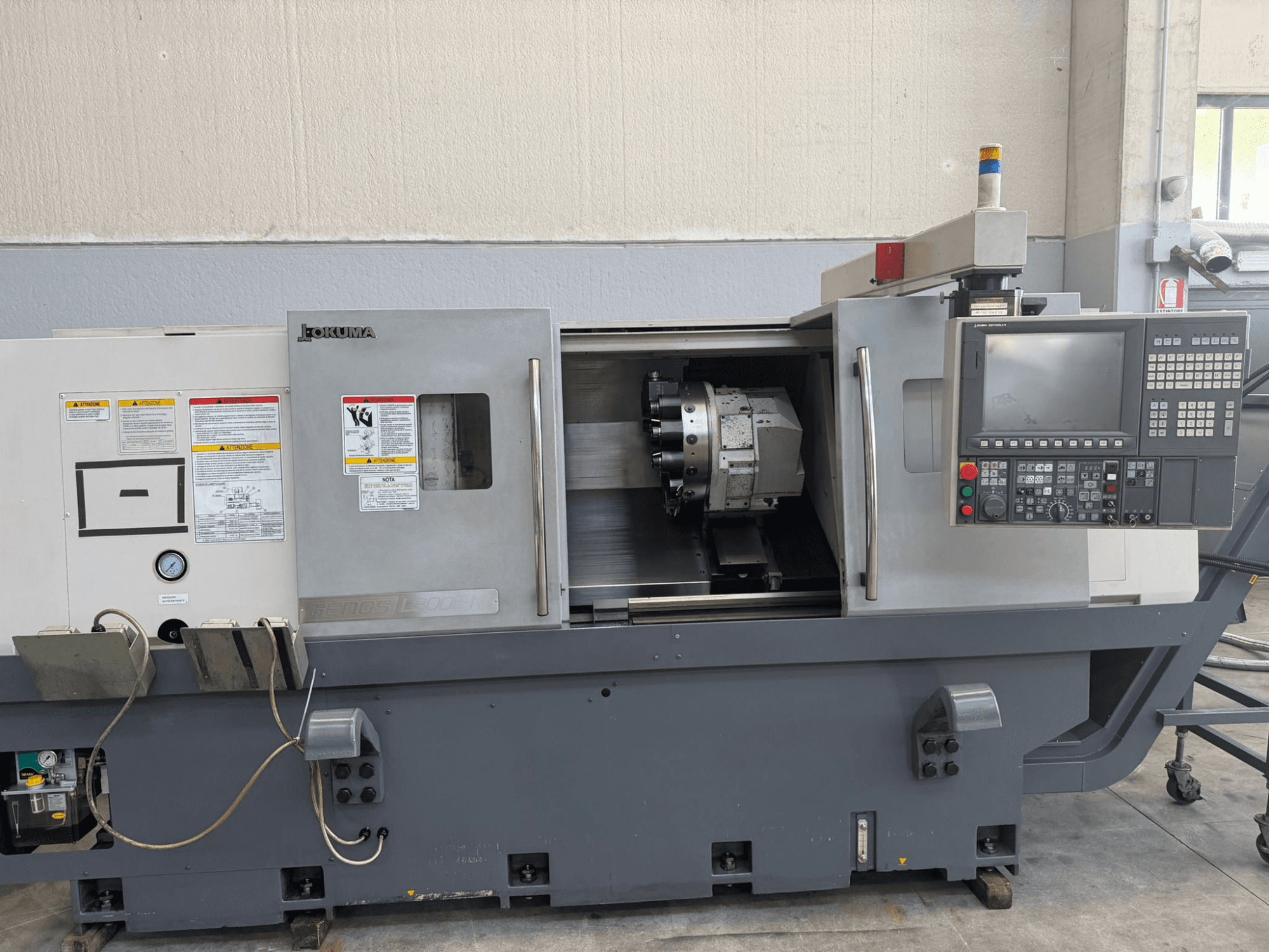 Tour CNC Okuma, vue de face, montrant le panneau de commande, le porte-outil de coupe et les avertissements de sécurité sur le côté.