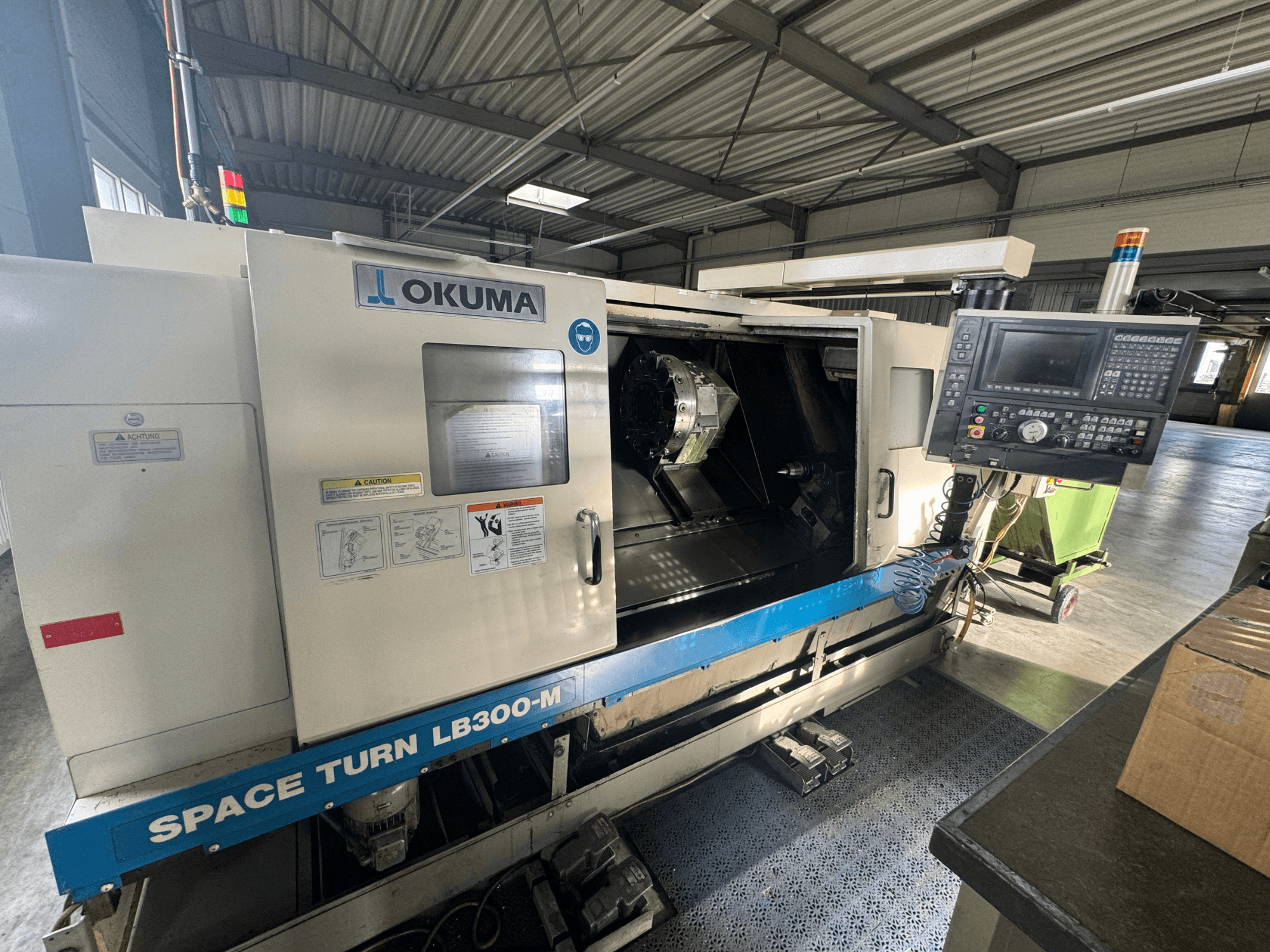 Tour CNC Okuma Space Turn LB300-M vu de face, avec panneau de commande et porte ouverte révélant la zone d'usinage intérieure.