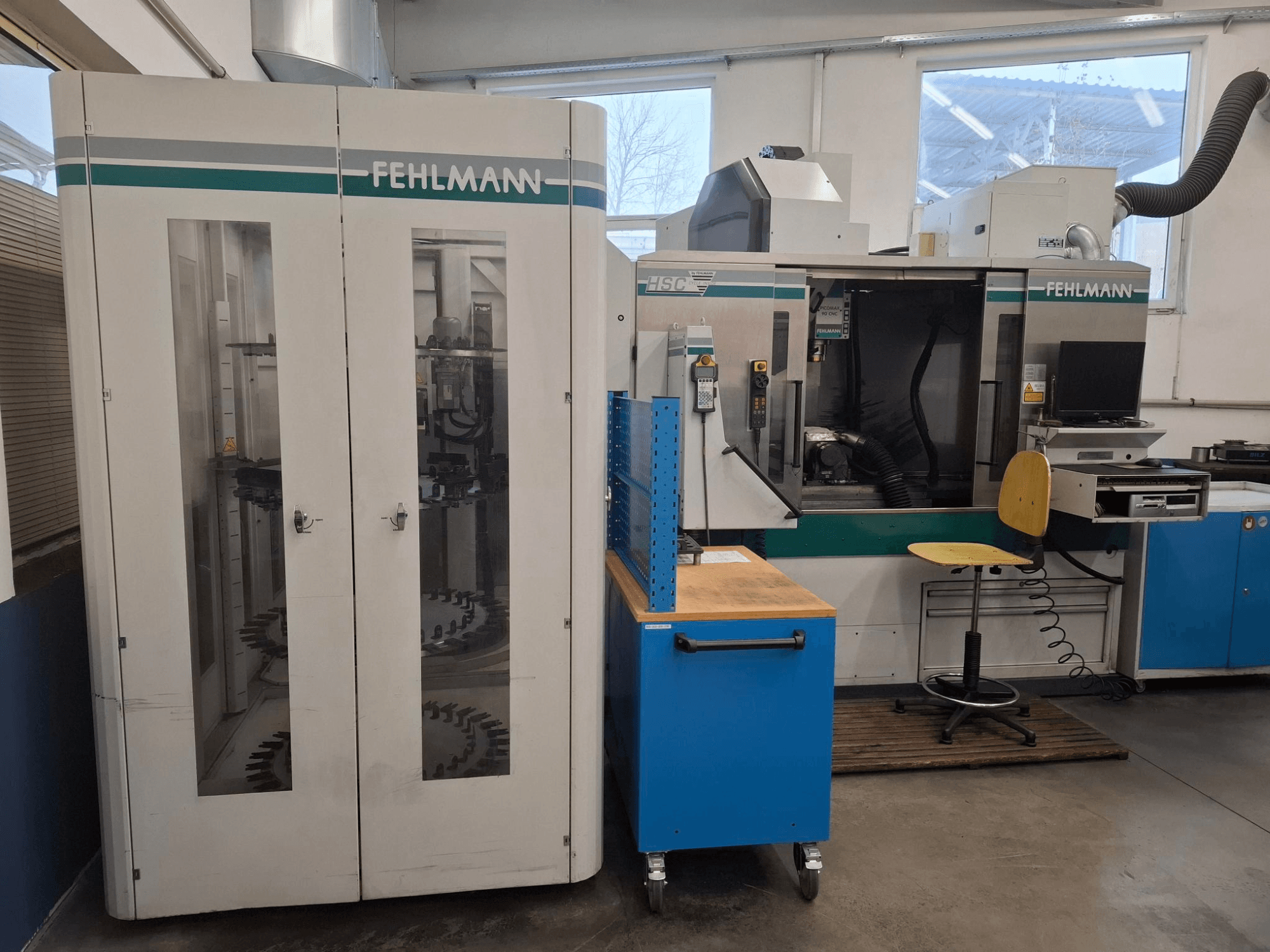 Centre d'usinage HSC FEHLMANN dans un atelier ; vue de face avec les commandes visibles, le siège et le rangement des outils.