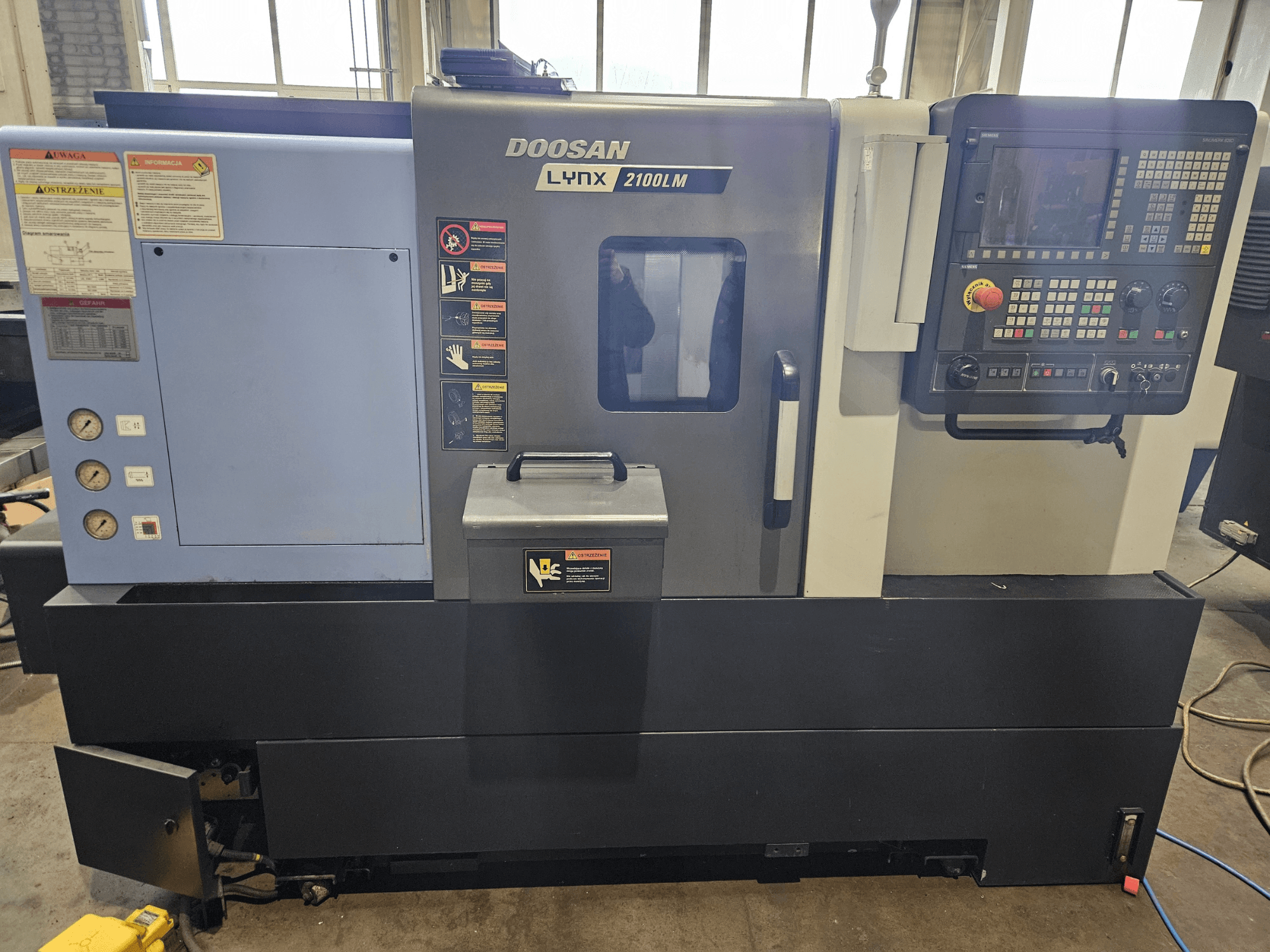 Tour CNC Doosan Lynx 2100LM, vue de face, avec panneau de commande, manomètres de pression d'air et étiquettes de sécurité visibles.