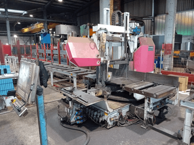 Machine à scier à ruban Behringer dans une usine, vue de face, avec une grande lame de coupe et un panneau de commande avec des boutons.