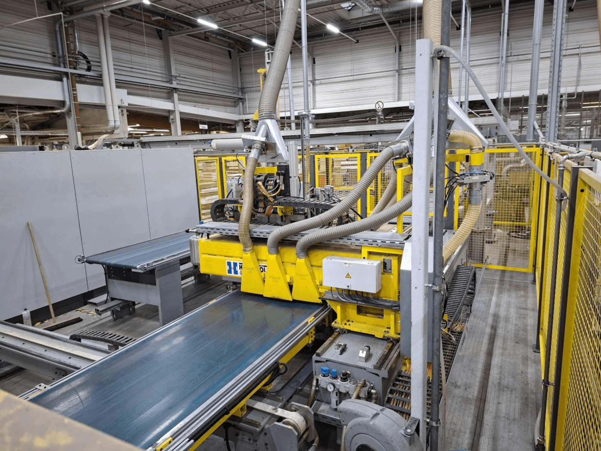 Système de convoyage industriel vu de côté, comprenant des machines jaunes, un panneau de commande et des tuyaux pour la fabrication.