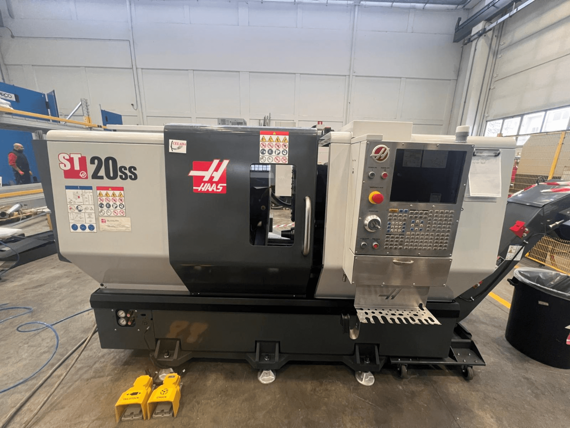 Tour CNC Haas ST 20SS en vue latérale, avec panneau de commande, étiquettes de sécurité et pédales au sol.