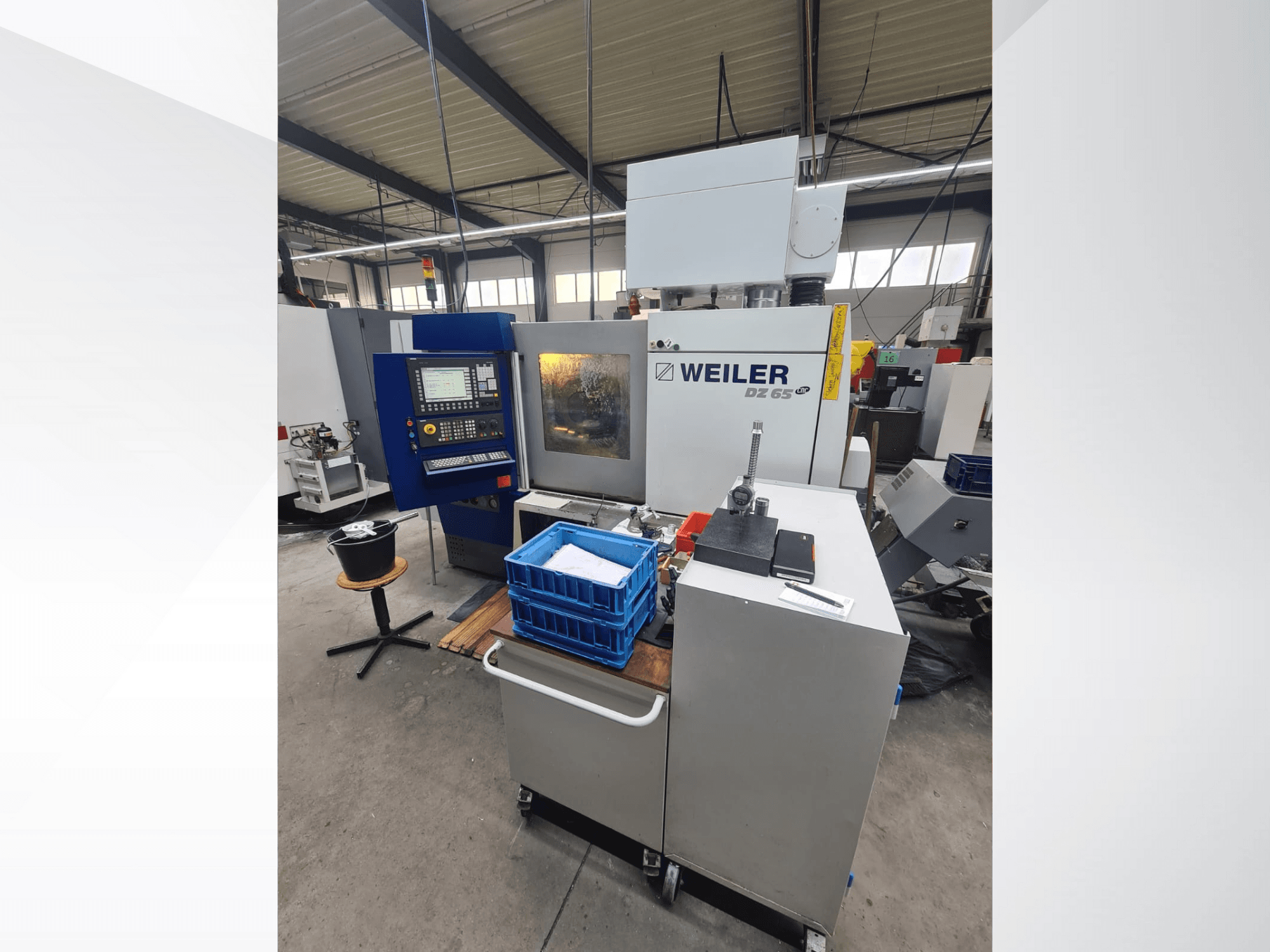 Machine CNC Weiler DZ 65 dans un atelier, vue de face avec le panneau de commande, les outils et les bacs de stockage bleus visibles.