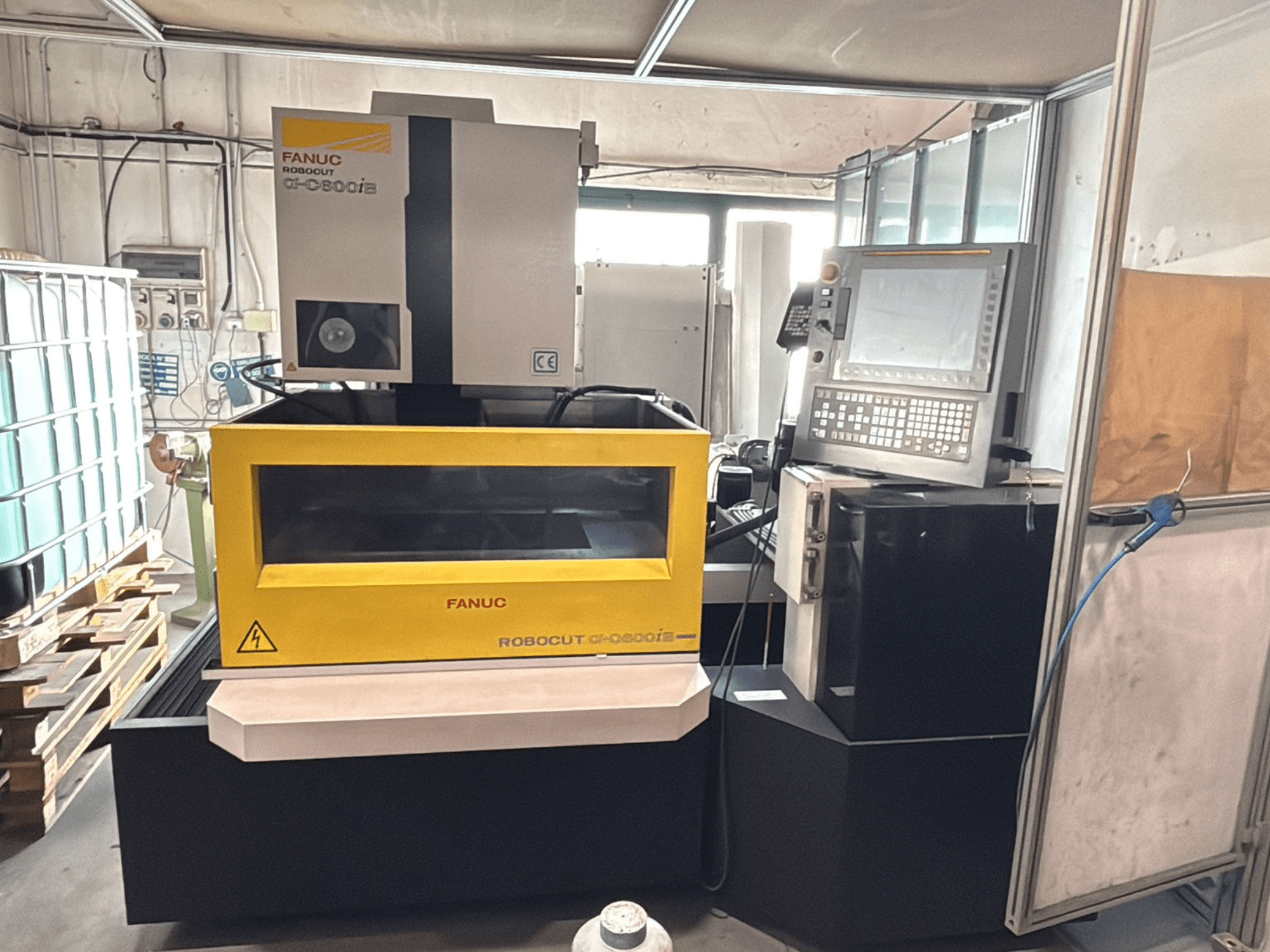 Vue avant d'une machine CNC FANUC Robocut α-0iE avec un boîtier jaune, montrant le panneau de commande et l'écran.