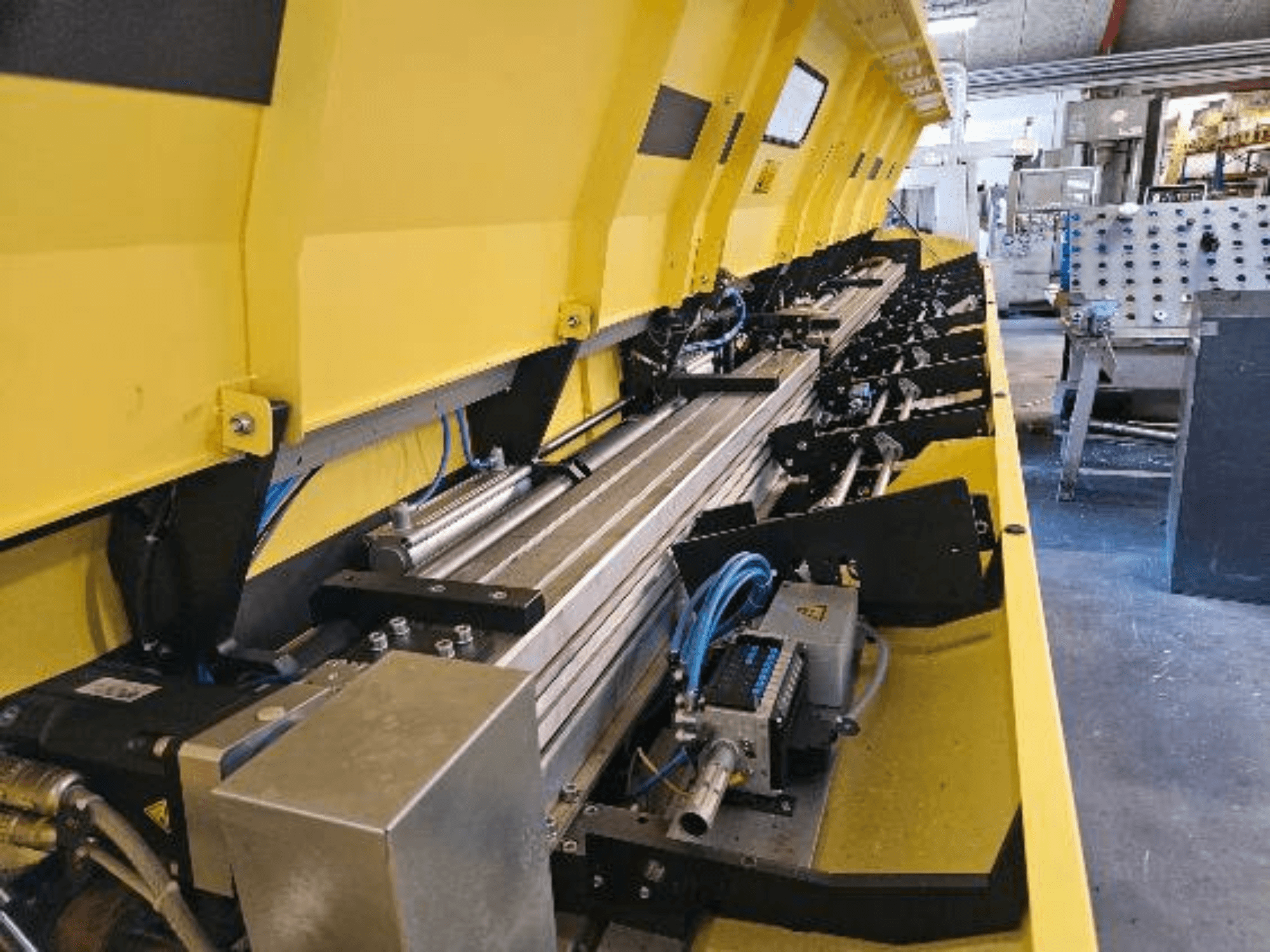 Vue rapprochée d'une machine hydraulique jaune avec des composants métalliques et des pistes de convoyage, avec des tuyaux et des pièces électroniques.