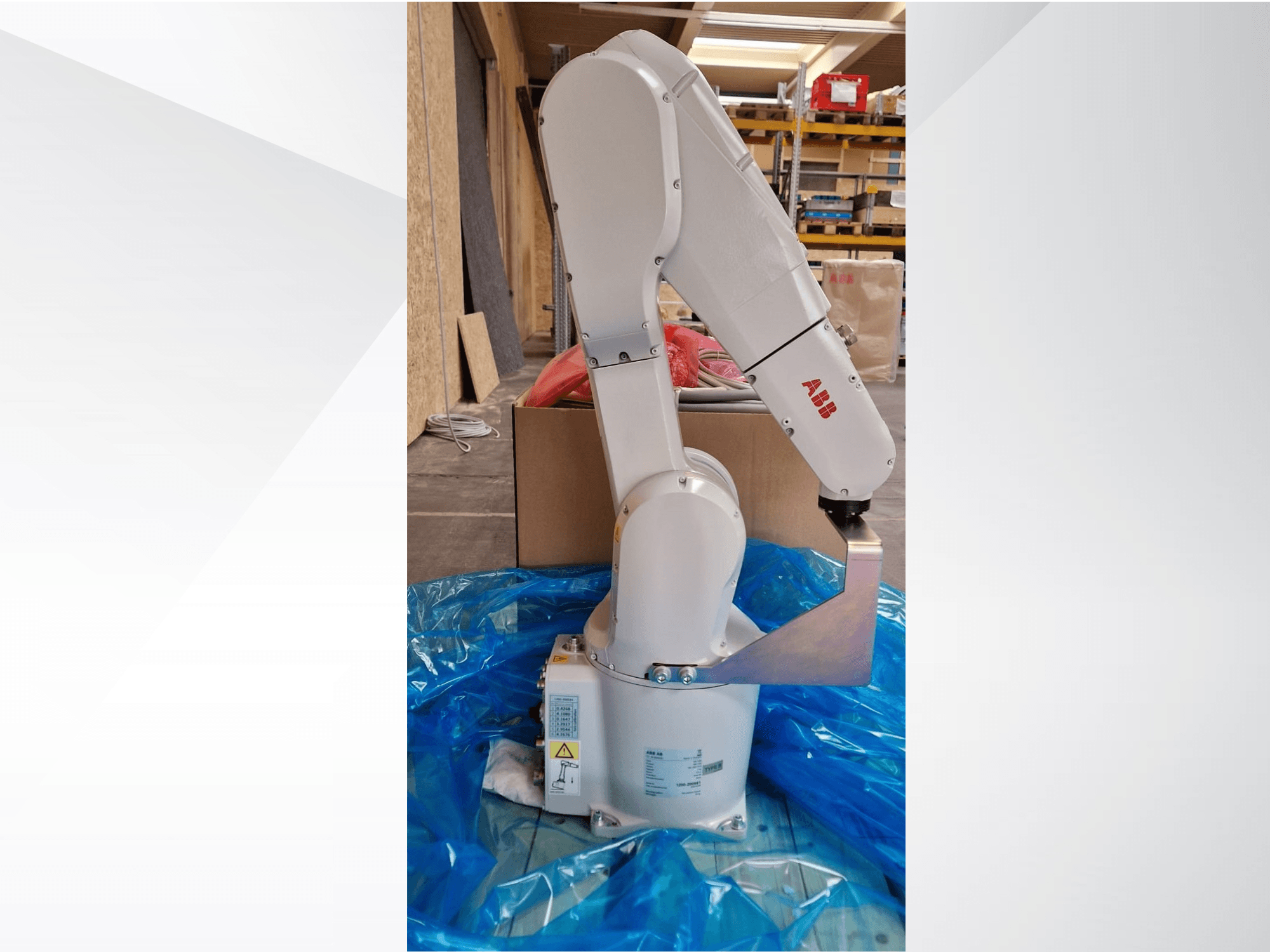 Modèle de bras robotique ABB, vue latérale sur bâche bleue, présentant les articulations et l'effecteur métallique, avec étiquettes techniques visibles.