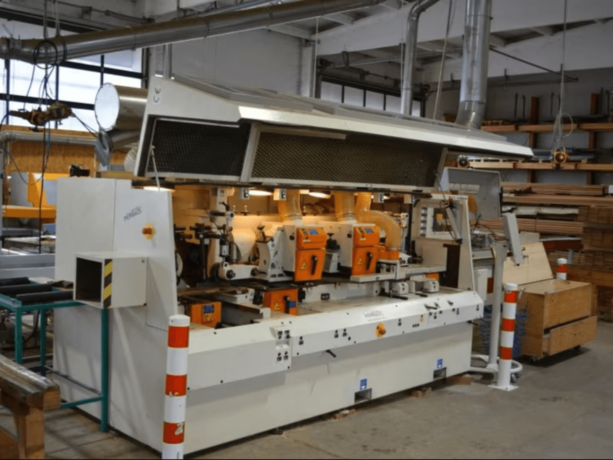 Machine de traitement du bois PENIGAS, vue de face, équipée de deux têtes de coupe orange et d'un système d'aspiration des poussières dans un atelier.