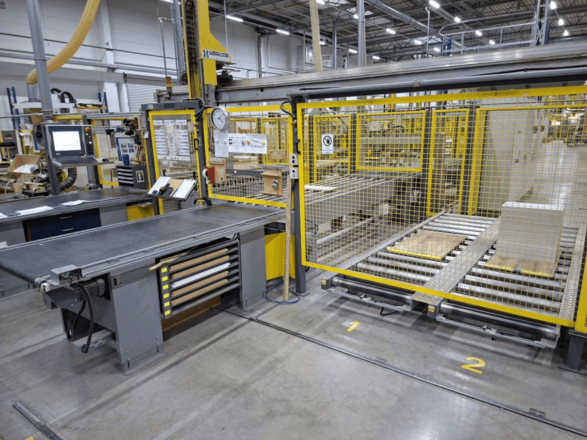 Espace de travail industriel comprenant un système de convoyage et un panneau de commande ; vue latérale montrant les machines et les clôtures de sécurité.
