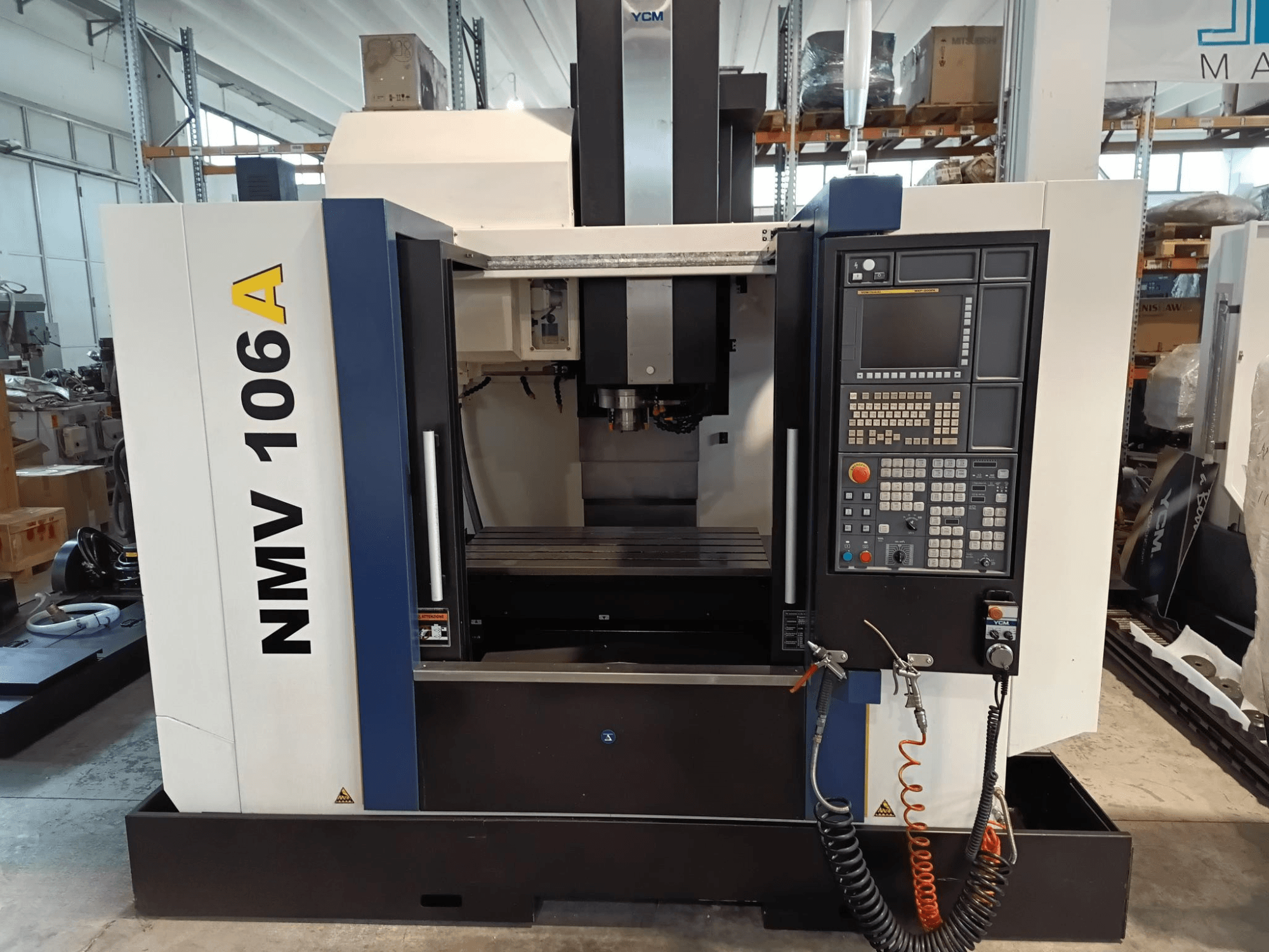 Centre d'usinage YCM NMV 106A, vue de face, panneau de commande avec boutons et tuyaux d'arrosage.