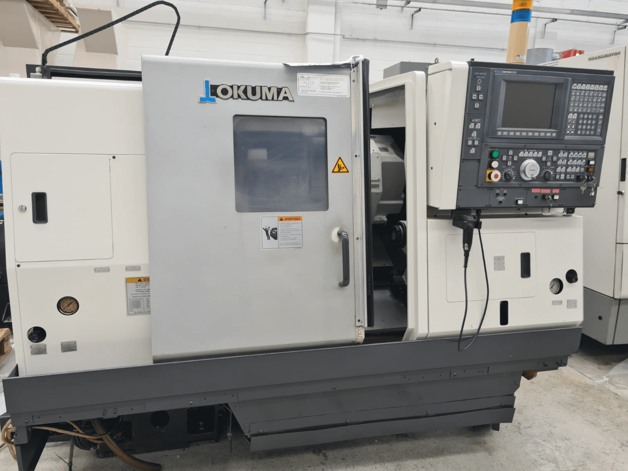 Tour horizontal Okuma LB 300M X 500 en vue latérale, présentant le panneau de commande, l'accès à la broche et les avertissements de sécurité.