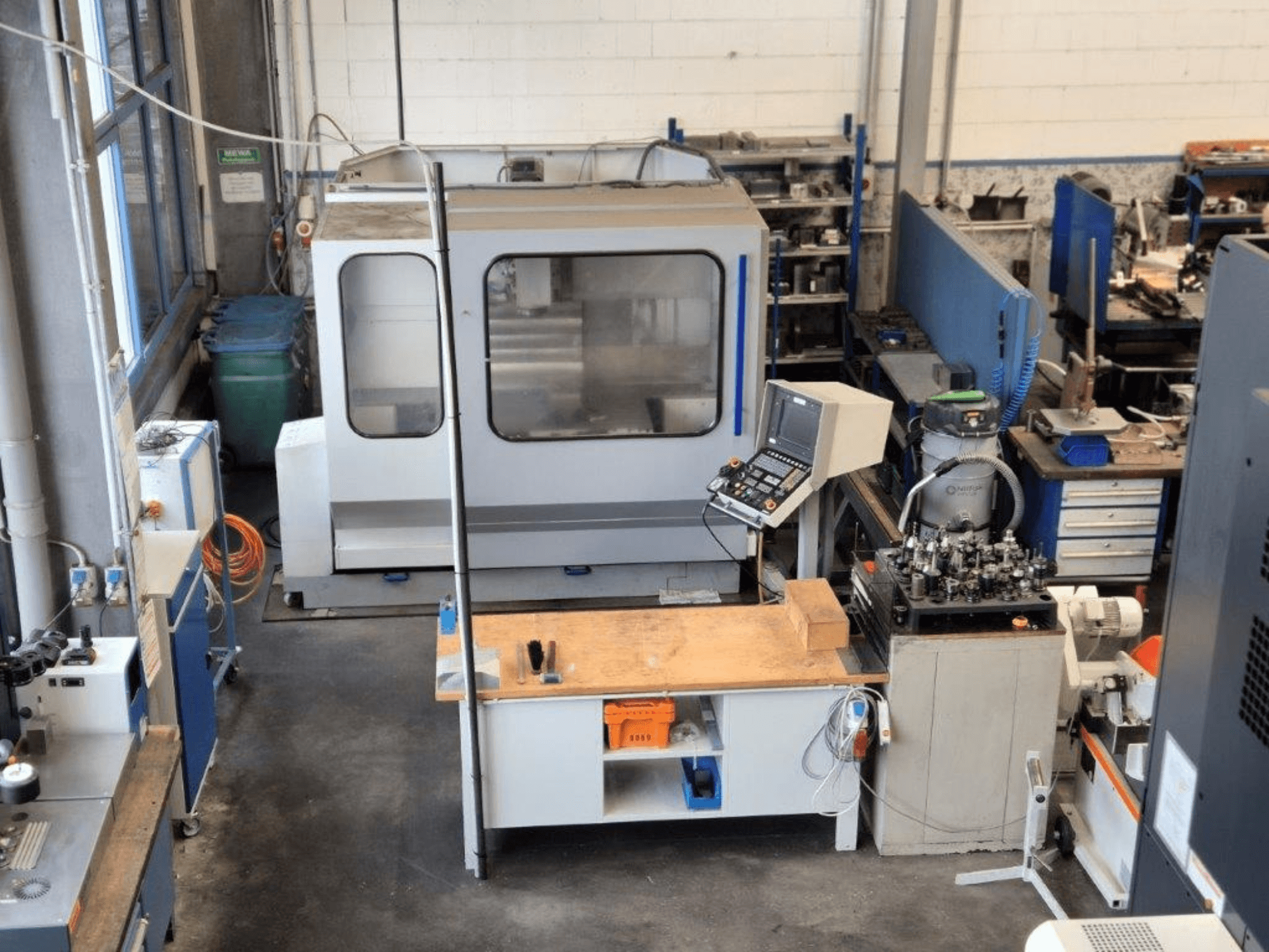 Fraiseuse à commande numérique dans un atelier, vue de face, avec panneau de commande, surface de travail et outils visibles à l'arrière-plan.