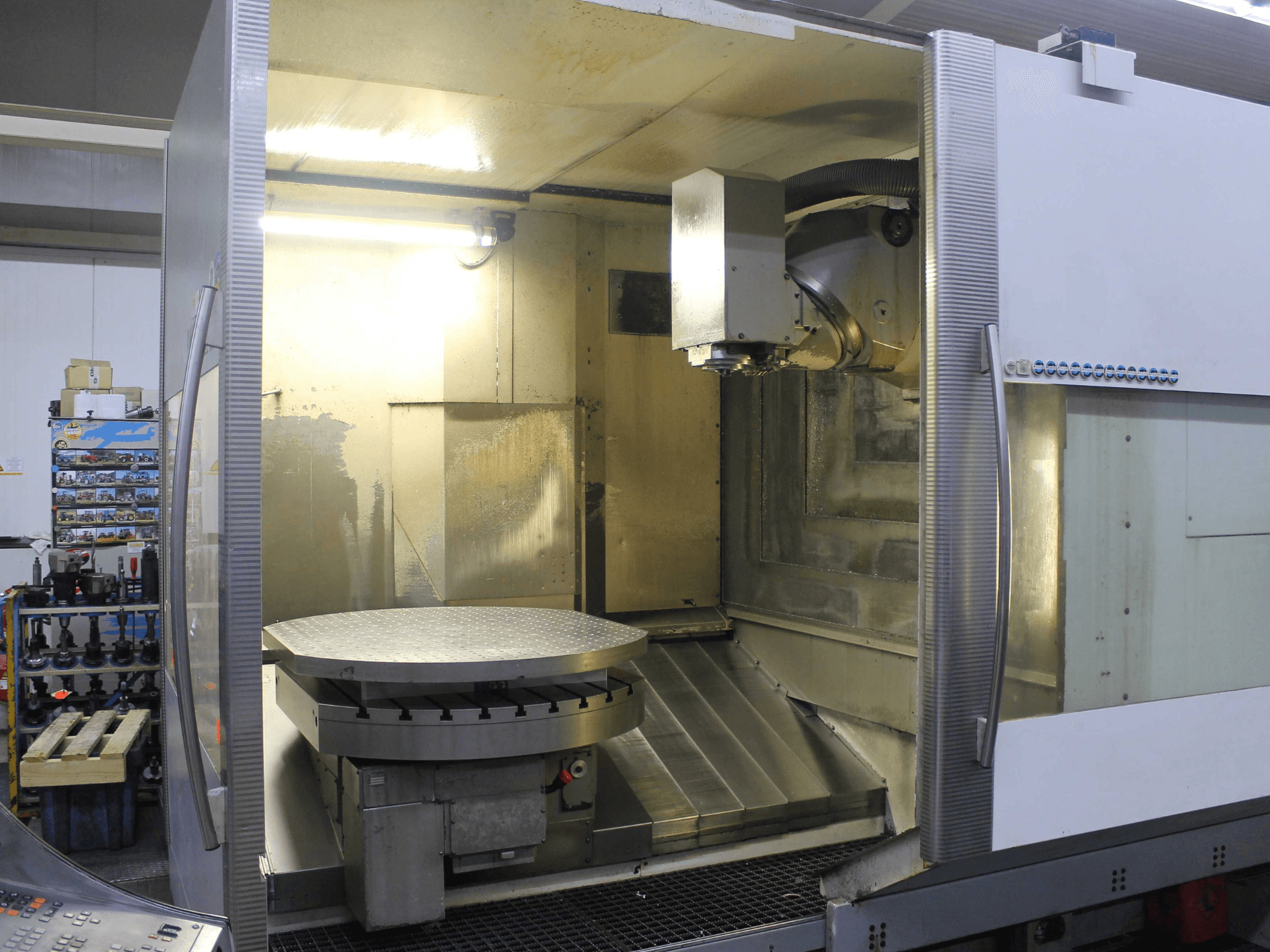 Fraiseuse CNC avec table rotative circulaire et tête de coupe, vue de face, avec surfaces métalliques et éclairage.