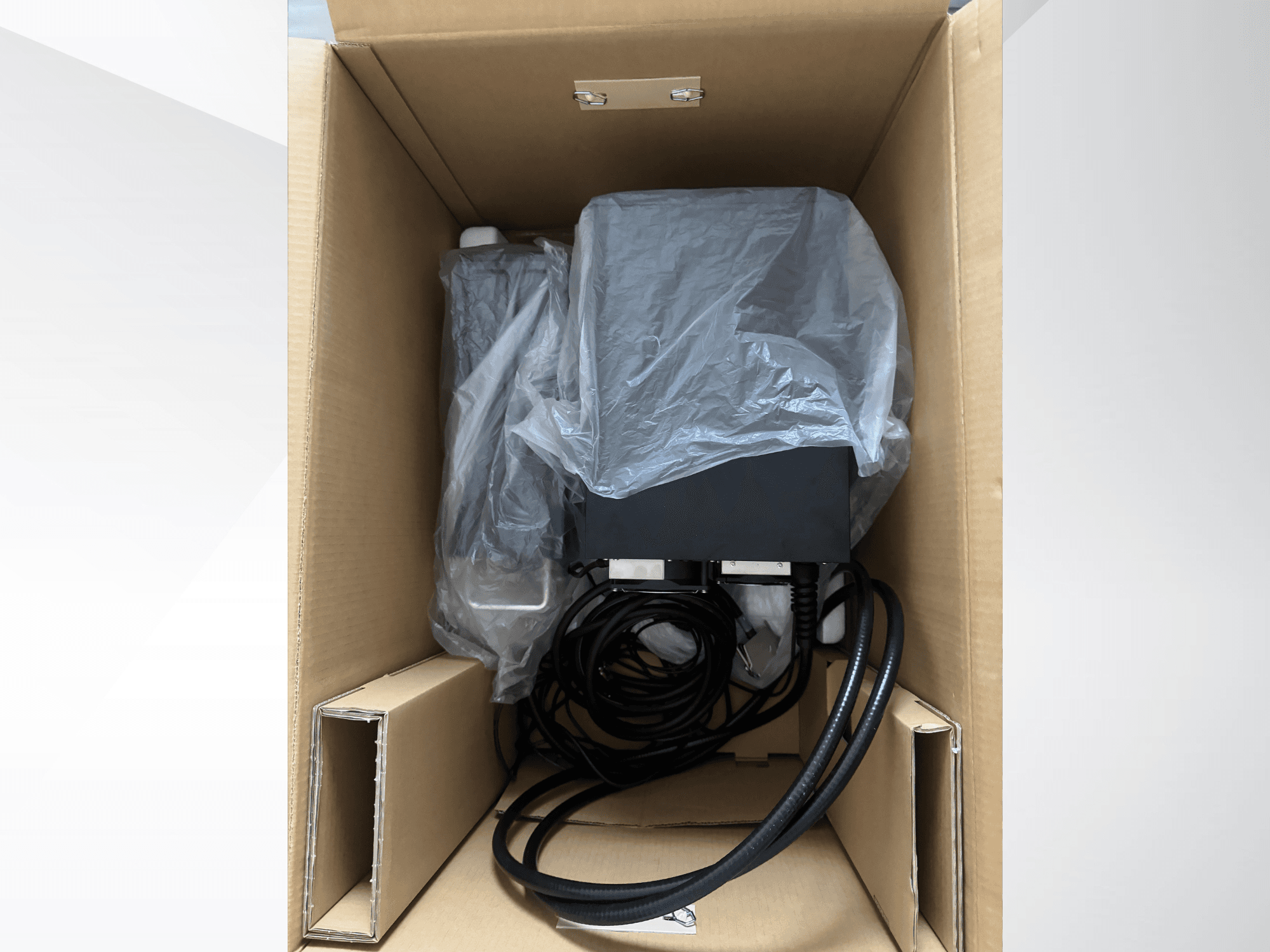 Machine de marquage laser KEYENCE MD-X2500A dans un carton, partiellement recouverte d'un film plastique, laissant apparaître les câbles et les composants.