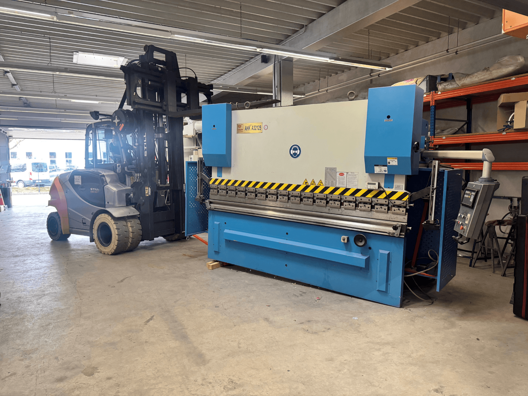 Presse hydraulique KNUTH AHK A 32125 dans un atelier, vue latérale montrant le panneau de commande et les dispositifs de sécurité.