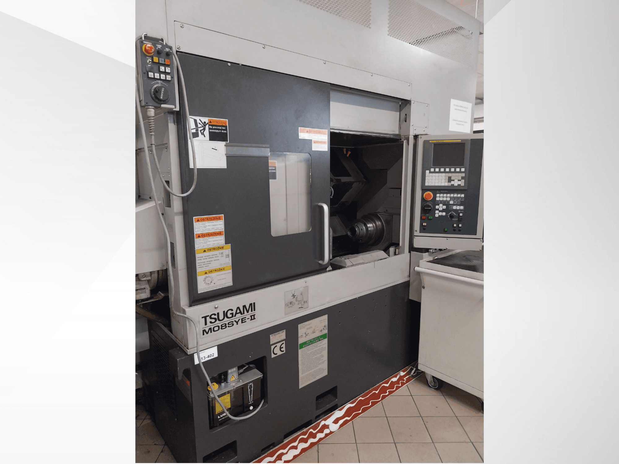 Tour CNC Tsugami M08SY-II, vue de face, montrant le panneau de commande, la broche et la zone de chargement. Présence d'avis de sécurité et d'une étiquette de marque.