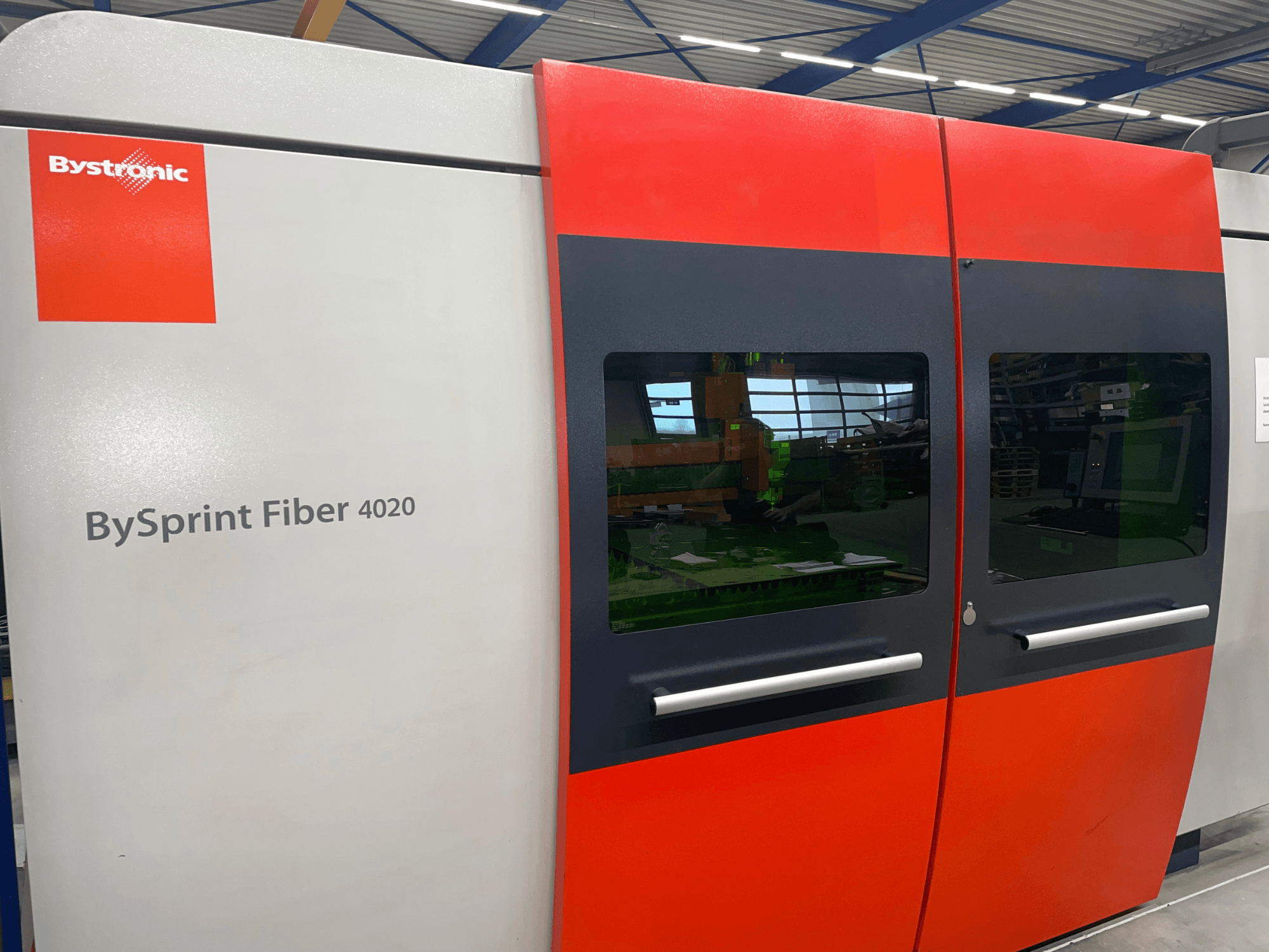 Bystronic BySprint Fiber 4020 en vue de face, avec un design de panneau gris et rouge avec de grandes fenêtres et une interface de contrôle visible à l'intérieur.