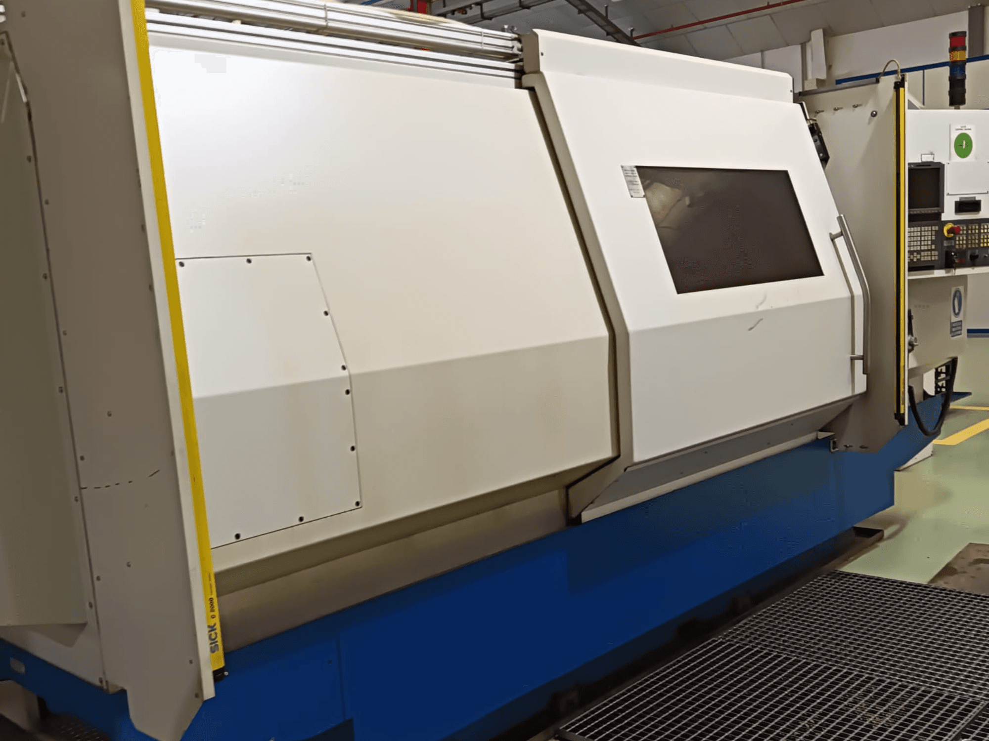 Tour industriel, vue latérale, avec un grand boîtier blanc et bleu, un panneau de commande numérique et des dispositifs de sécurité.