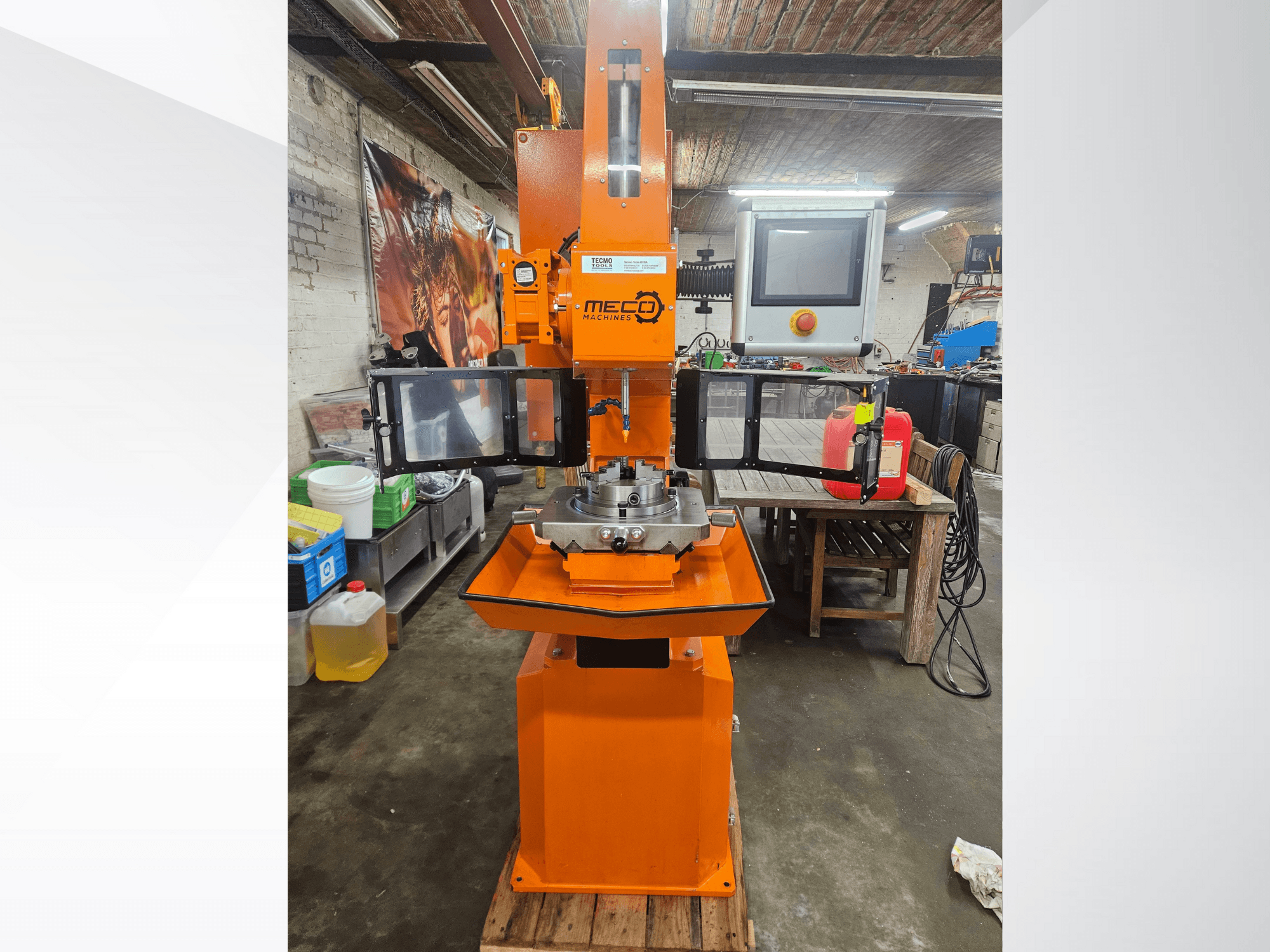 Fraiseuse orange MEC, vue de face, avec panneau de commande et table de travail, située dans un atelier avec outils et matériaux.