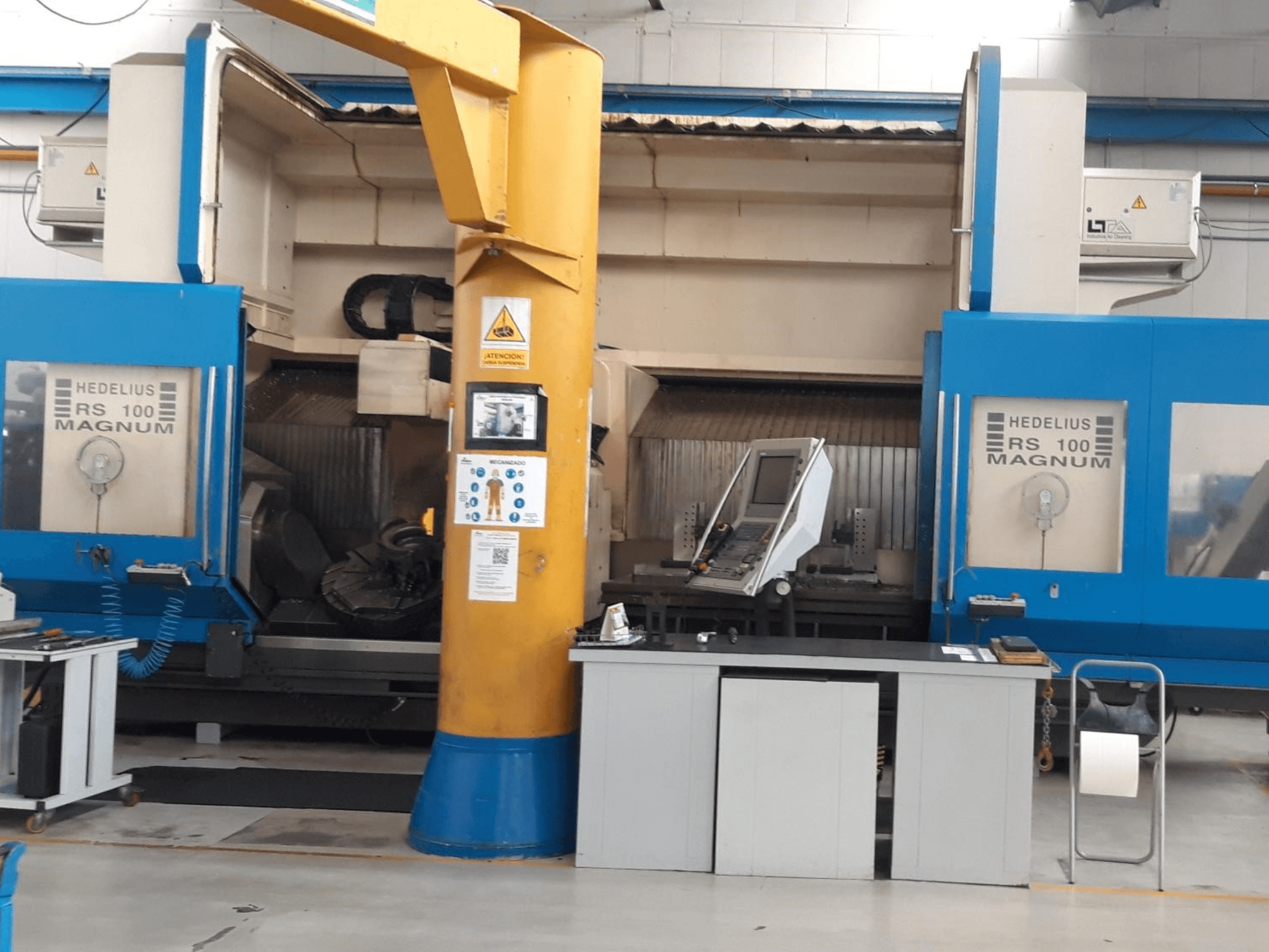 Machine HEDALIUS RS 100 MAGNUM, vue de face ; elle comporte un panneau de commande et une colonne de support jaune, dans un espace de travail industriel.