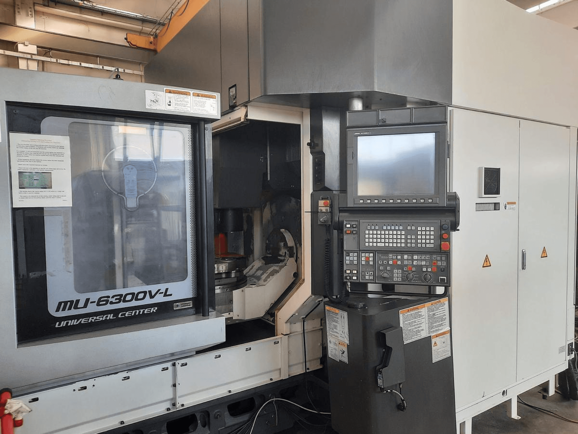 La machine MU-6300V-L Universal Center est présentée de face, avec le panneau de commande, l'écran et les instructions opérationnelles visibles.