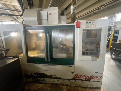 Centre d'usinage vertical Bridgeport VMC 1000/30, vue de face avec le panneau de commande, montrant l'extérieur usé et les portes vertes.