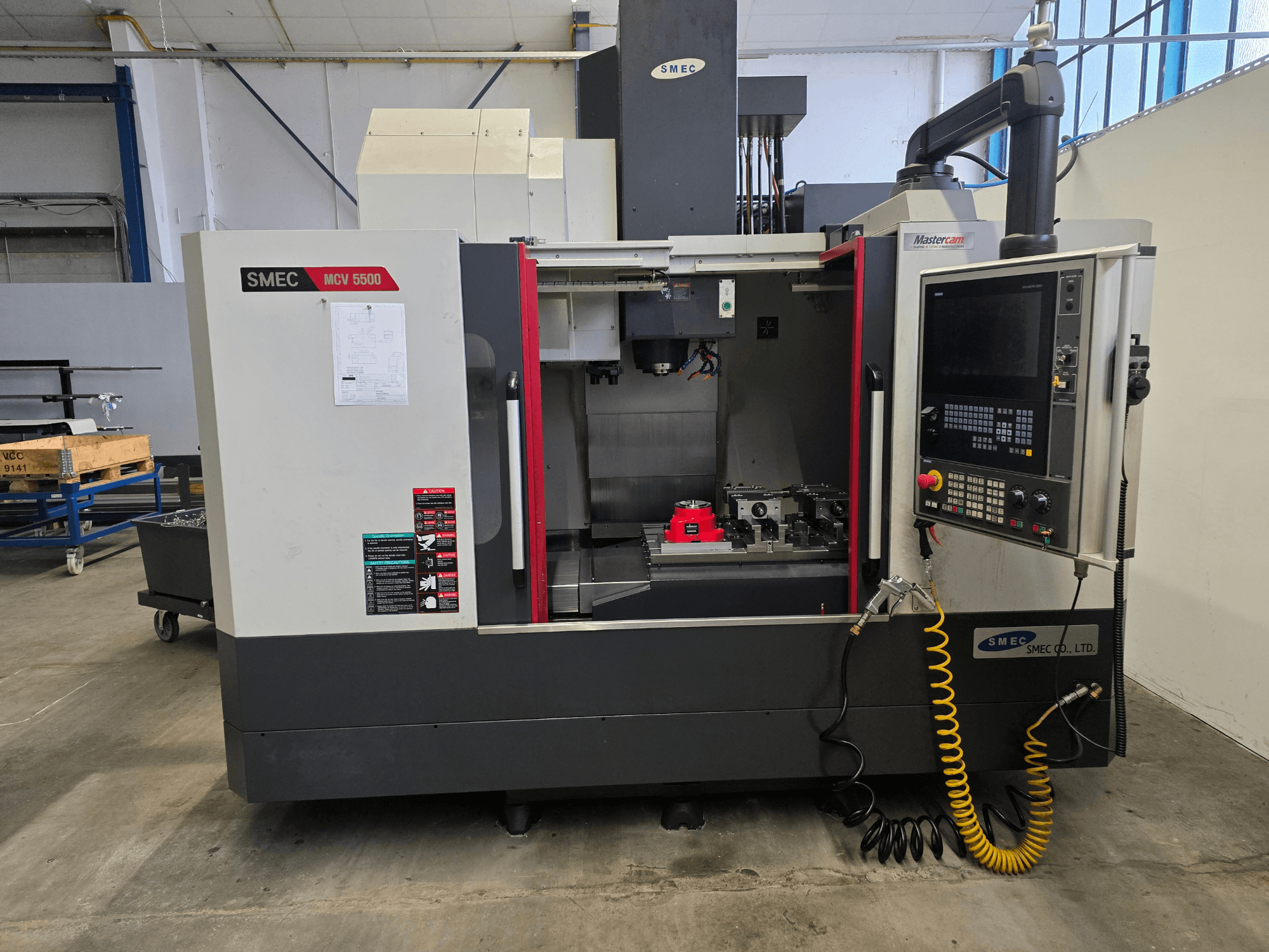 Centre d'usinage vertical SMEC MCV 5500, vue de face, montrant le panneau de commande et l'intérieur de la machine avec les outils.