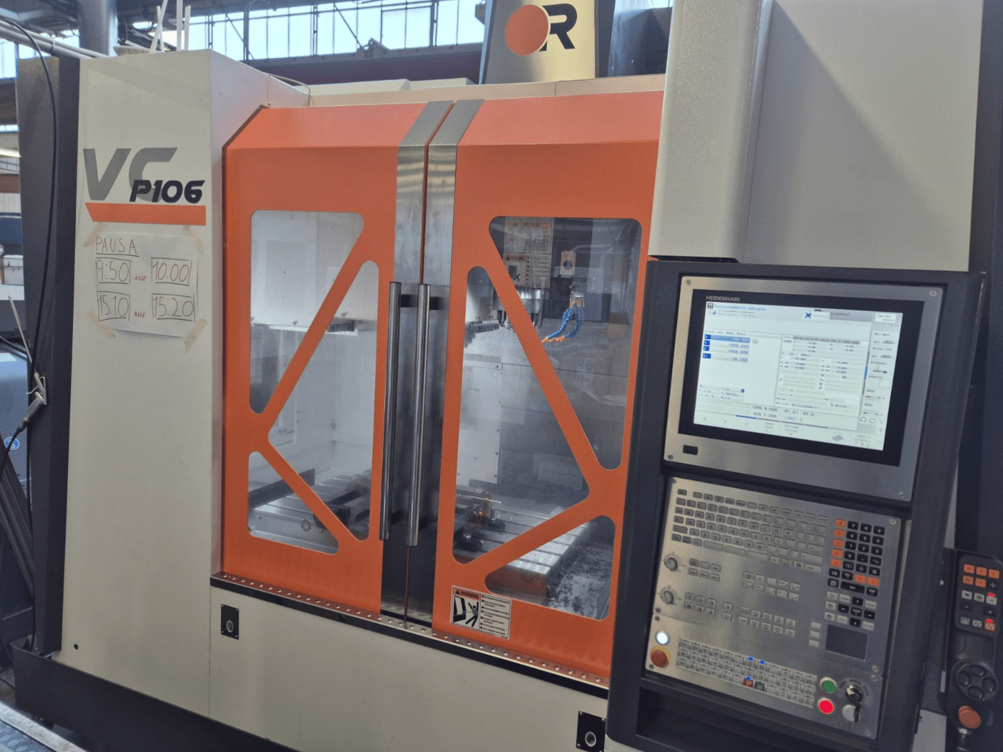 Texte alternatif : Machine CNC VF P106 orange et grise, vue de face, affichant un panneau de commande et des heures de fonctionnement programmées sur papier.