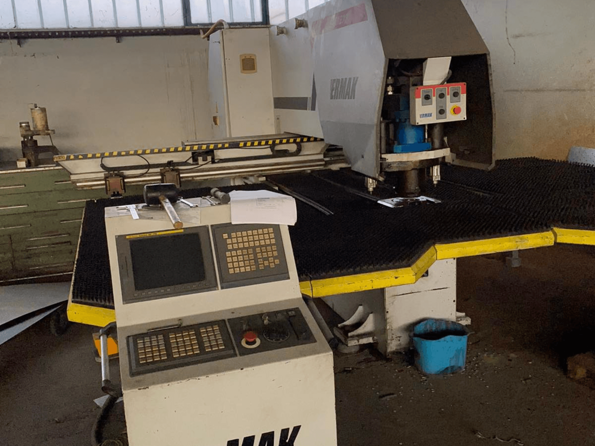 Machine CNC Ermak, vue de face, comprenant le panneau de commande, la tête de coupe sur un tapis en caoutchouc et les outils à proximité dans un environnement industriel.