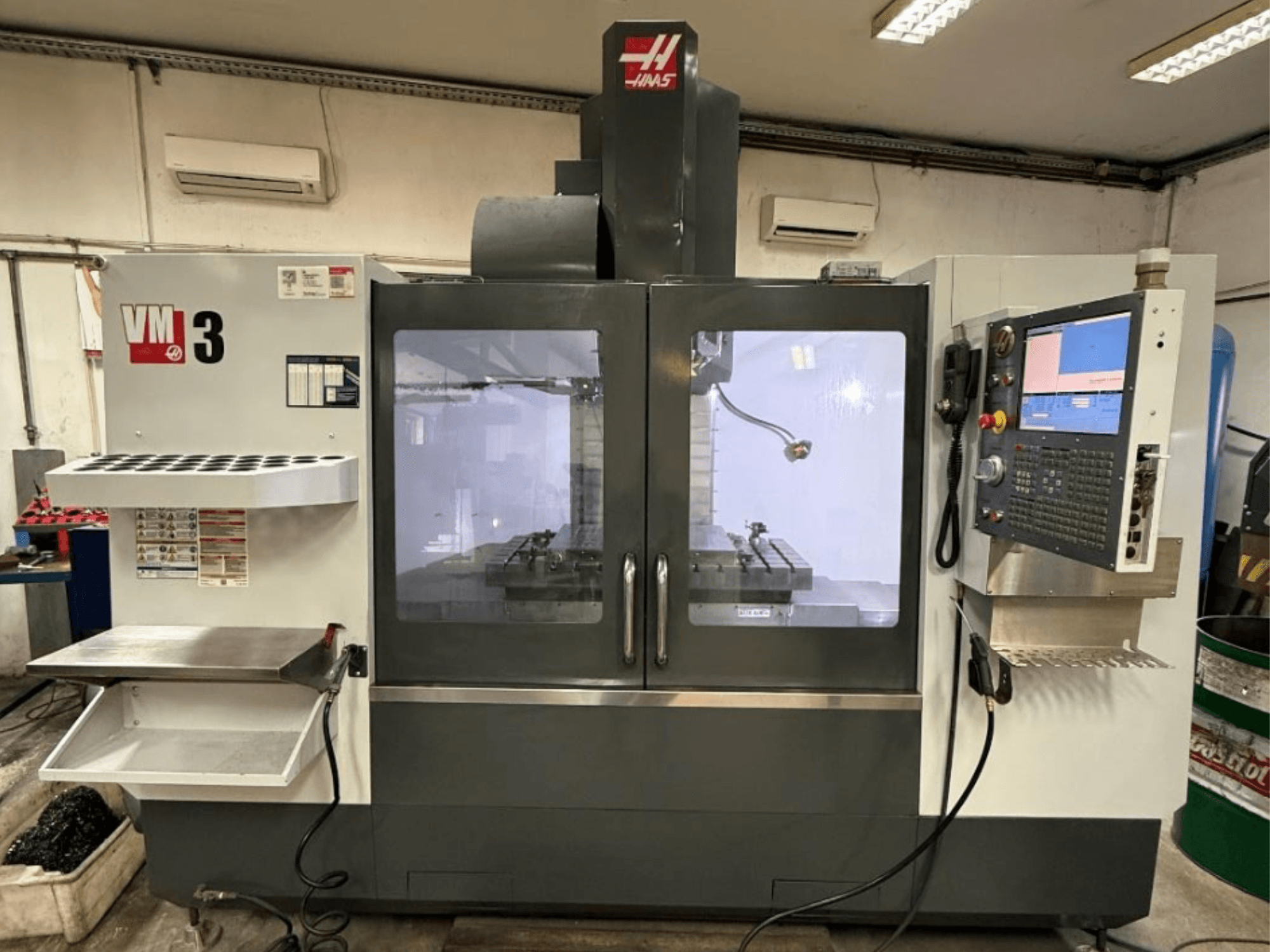 Centre d'usinage vertical Haas VM-3 vu de face, doté d'un grand panneau de commande et d'une zone de travail visible avec les outils.