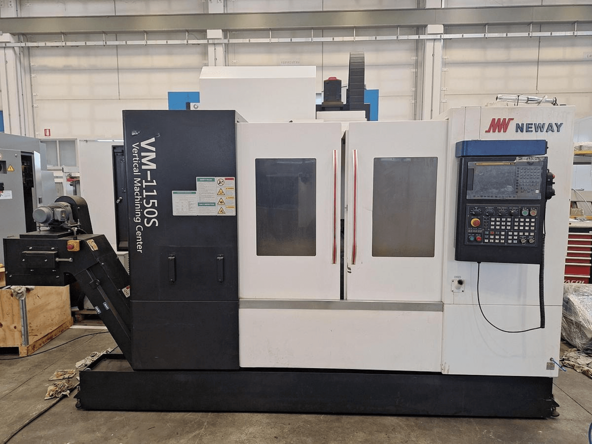 Centre d'usinage vertical Neway VM-1150S, vue de face montrant le panneau de commande, les portes et les étiquettes de sécurité.