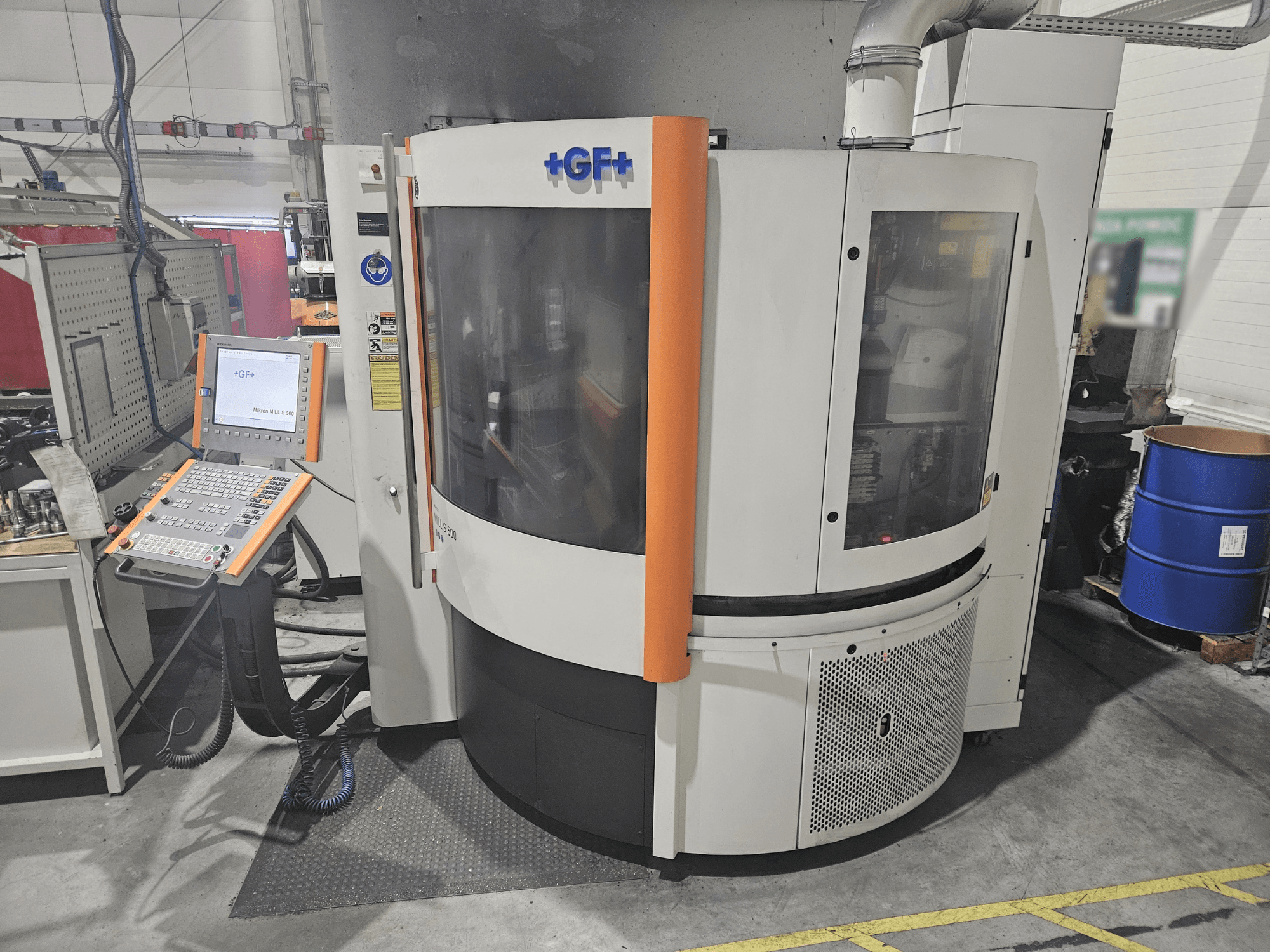 Machine-outil de GF Machining Solutions avec panneau de commande, vue de face ; panneau transparent, accents orange et environnement industriel.
