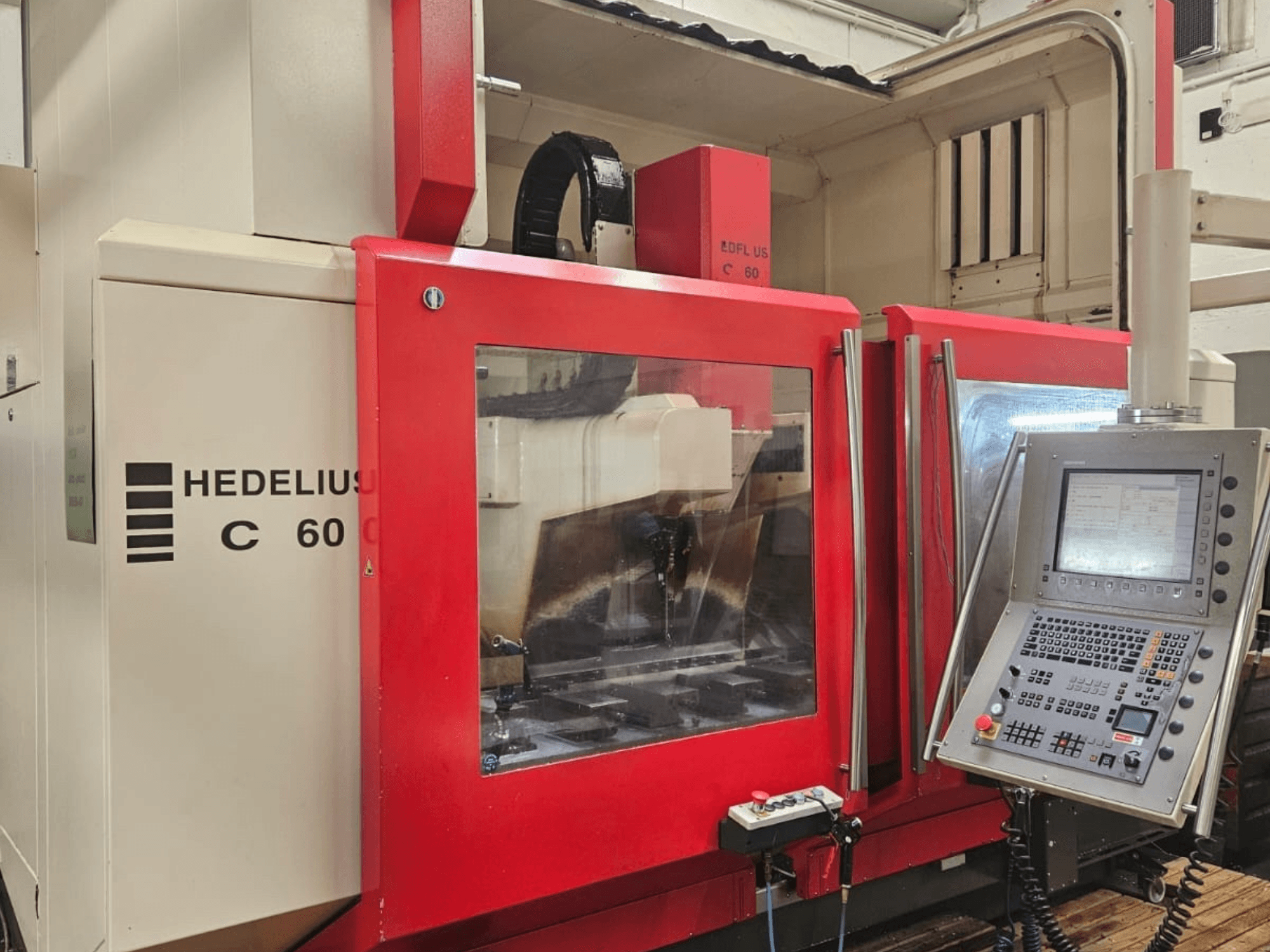 Centre d'usinage vertical HEDELIUS C60 vu de côté, avec un panneau frontal rouge et une console de commande avec écran.