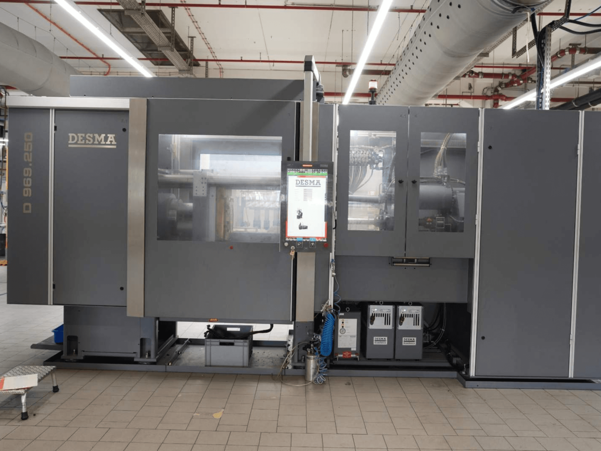 Machine de moulage par injection verticale Kloeckner Desma D 969.250 Z (S3) en milieu d'usine, vue de face avec le panneau de commande.