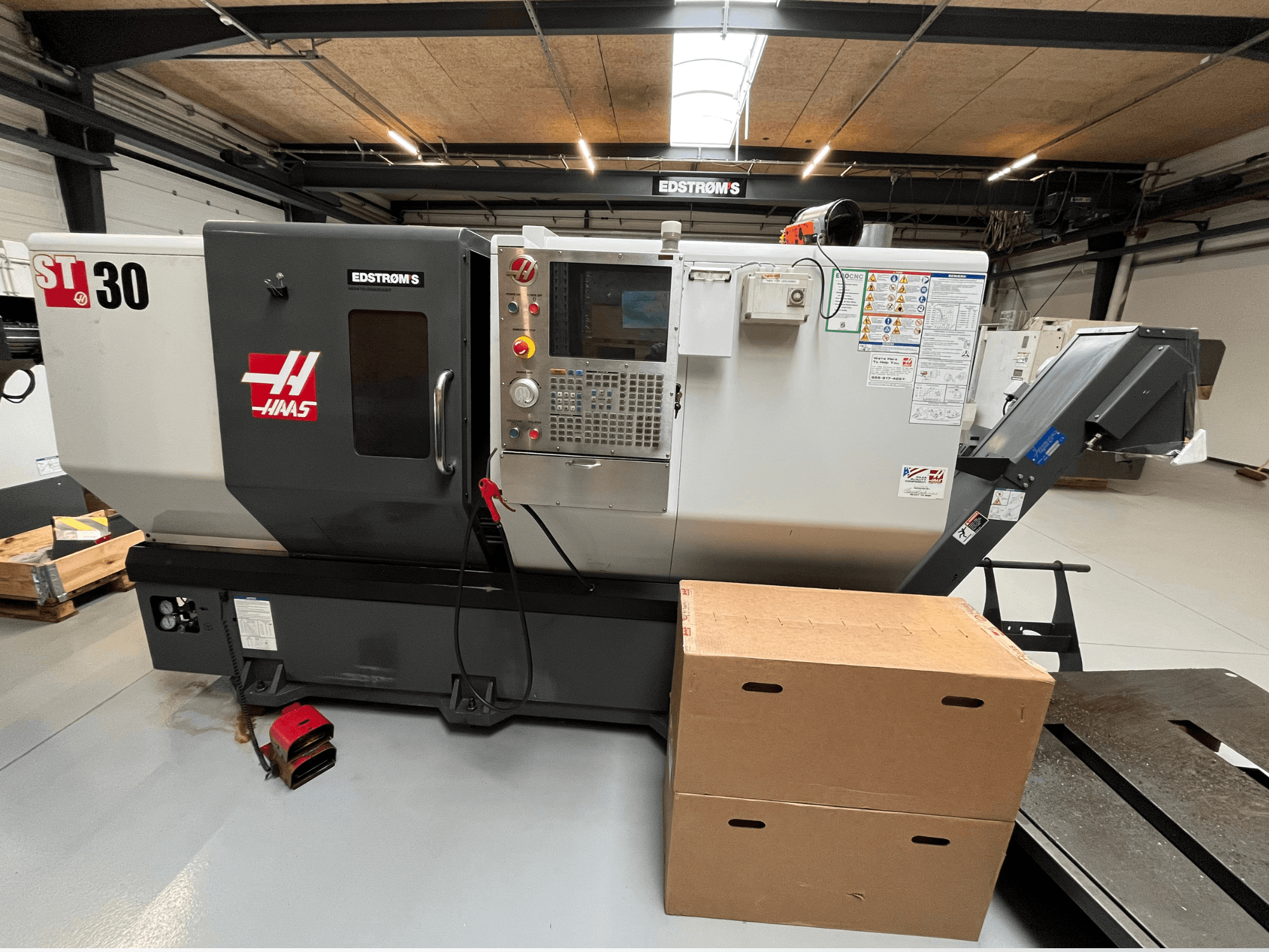 Tour CNC Haas ST-30 vu de côté, avec un panneau de commande, un badge de modèle et deux boîtes en carton à proximité.