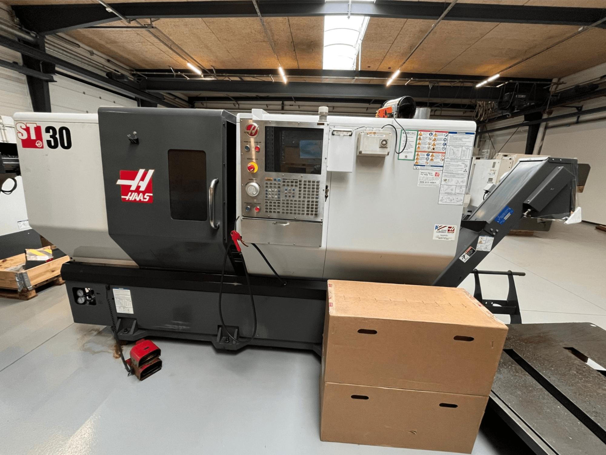 Tour CNC Haas ST-30, vue de face, panneau de commande avec boutons, arrêt d'urgence et deux boîtes en carton empilées.